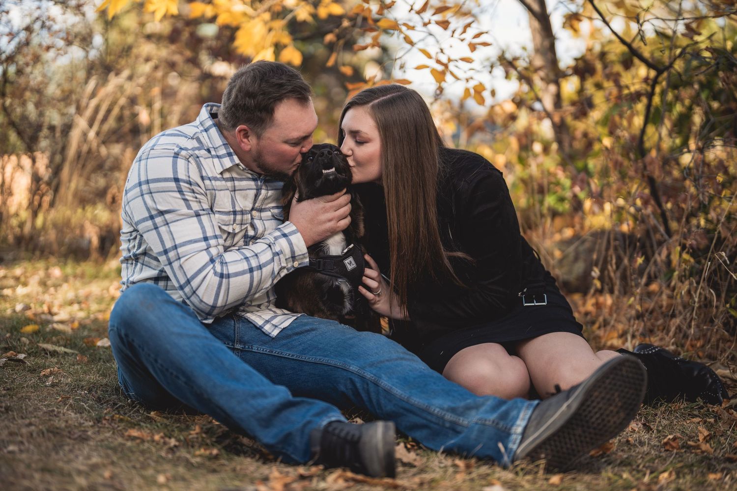 A couple sitting on fallen autumn leaves sharing a warm moment together.