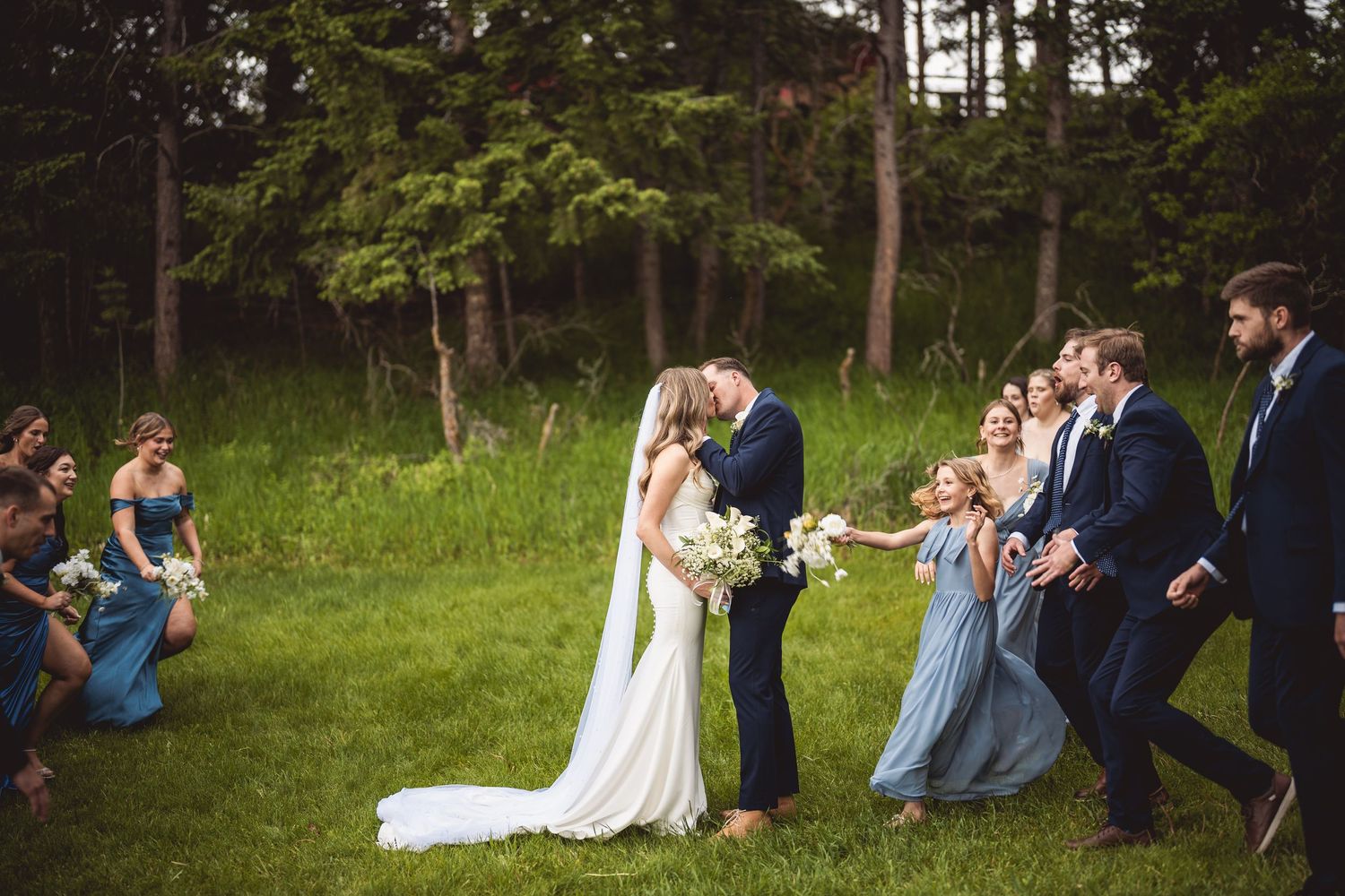 Outdoor wedding gathering with attendees in blue and white against forest backdrop.
