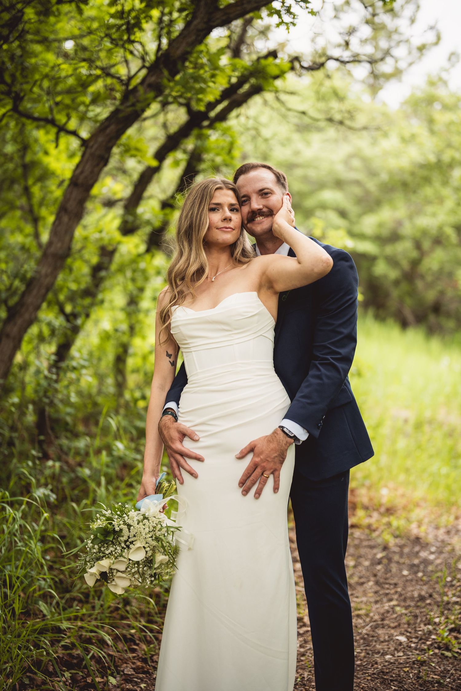 Intimate wedding portraits captured on natural wooded path with green backdrop.