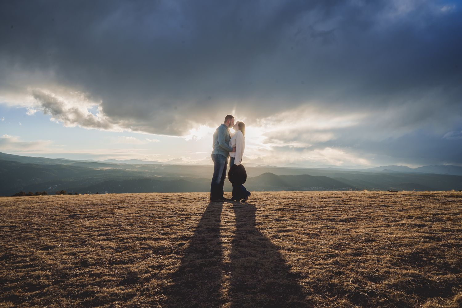 Dramatic cloudy sky frames couple walking across scenic mountain vista.