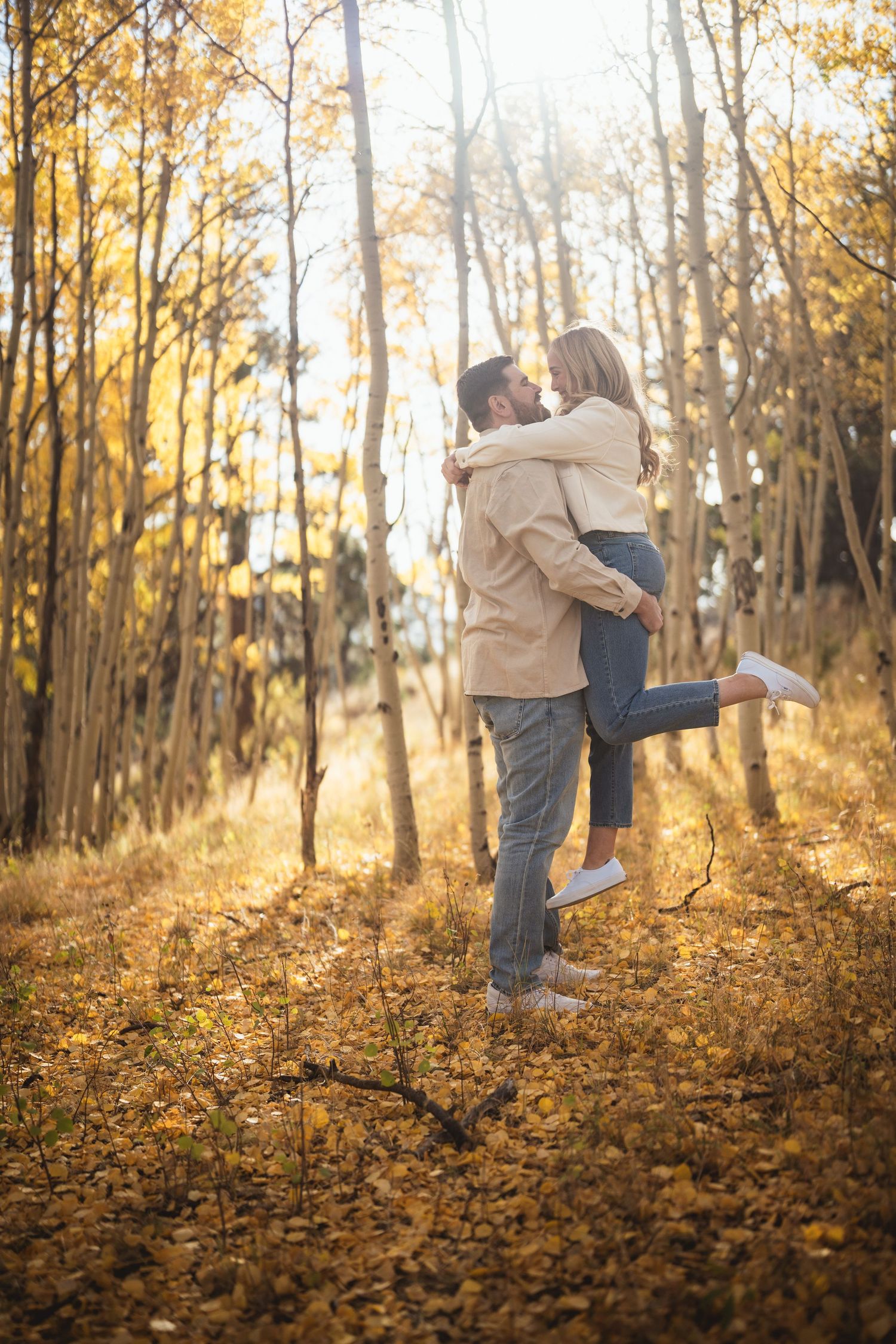 Couple playfully posing in a golden autumn forest with fallen leaves.