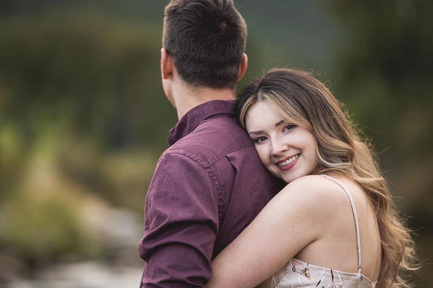 Couple embracing outdoors with soft natural lighting and green foliage backdrop.