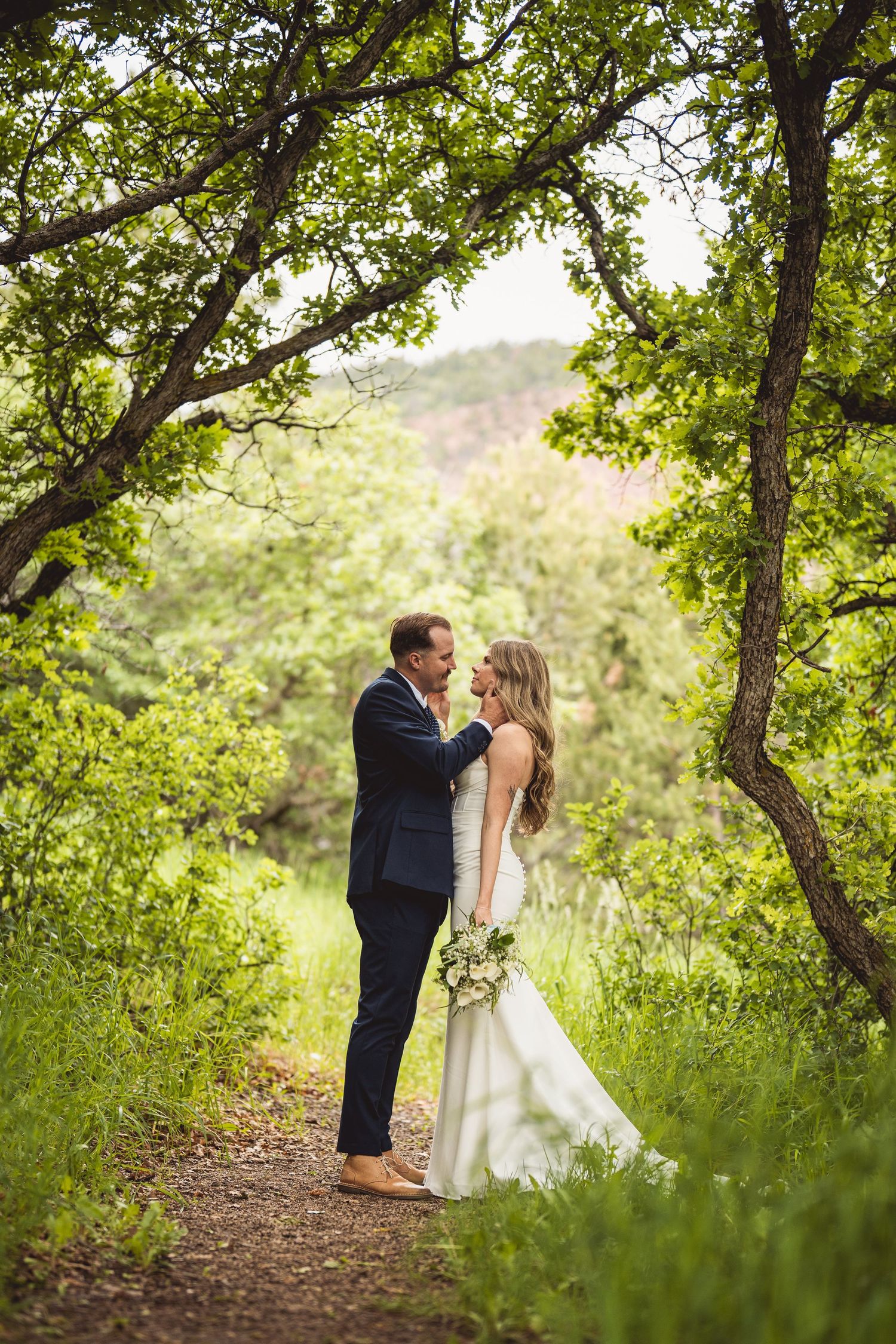 Romantic woodland wedding photo with couple embracing on a tree-lined path.