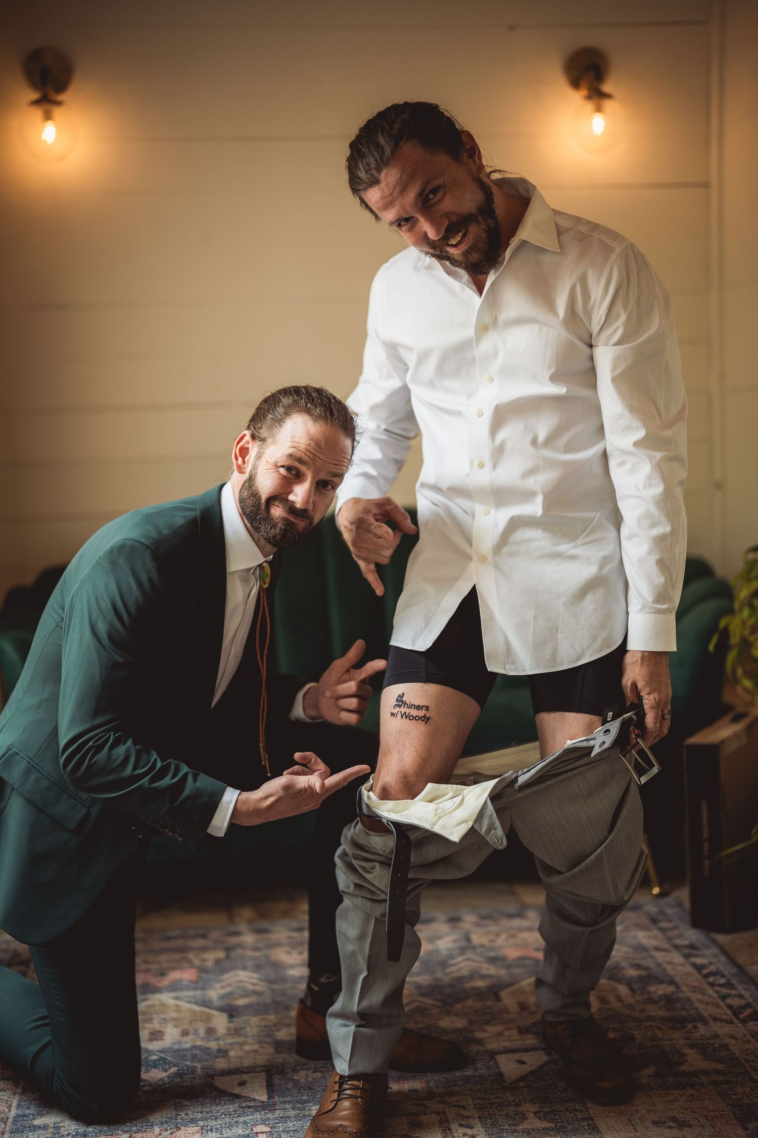 Groom getting help with formal attire preparations on patterned carpet.