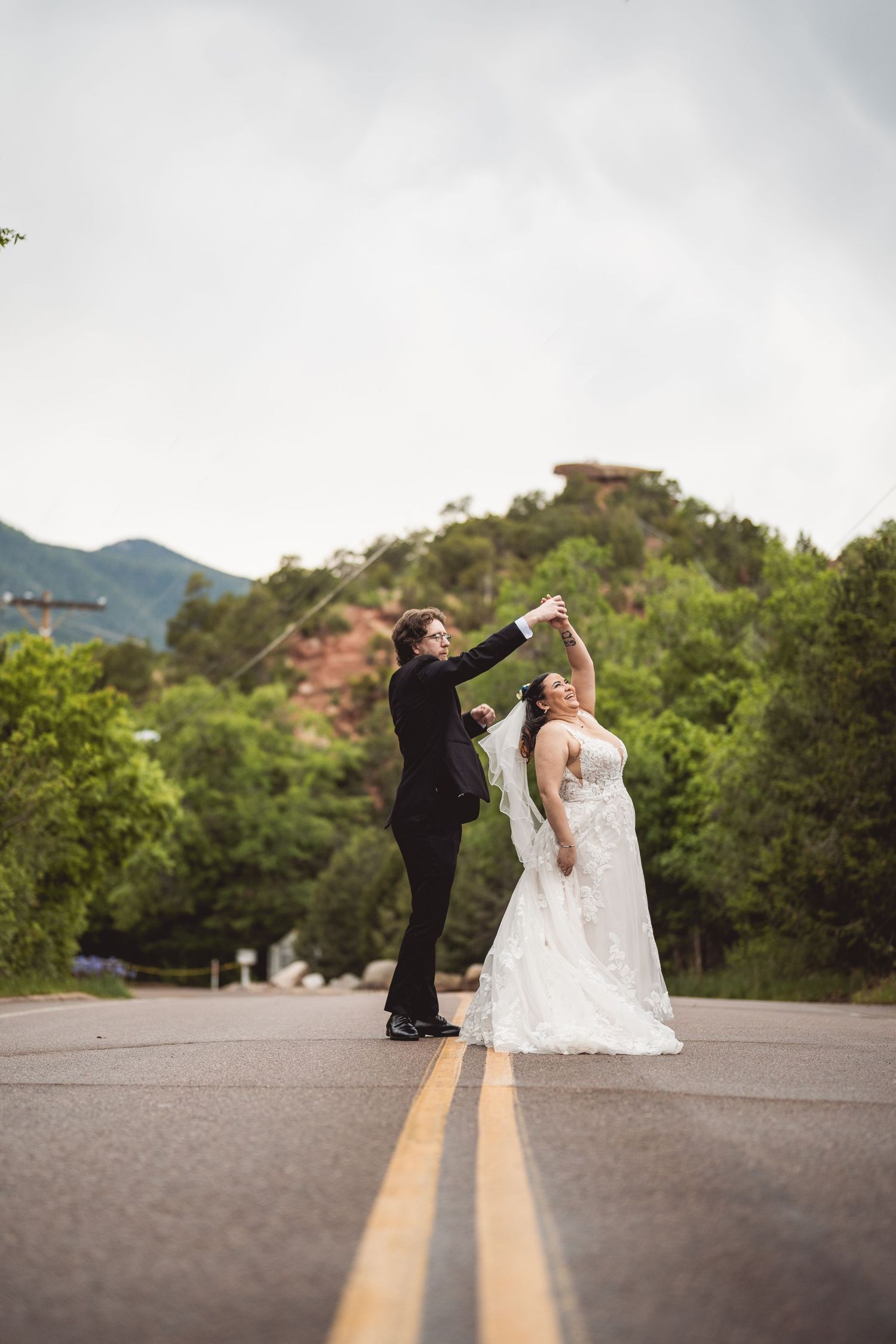 Wedding couple dances playfully on a mountain road during their outdoor photo session.