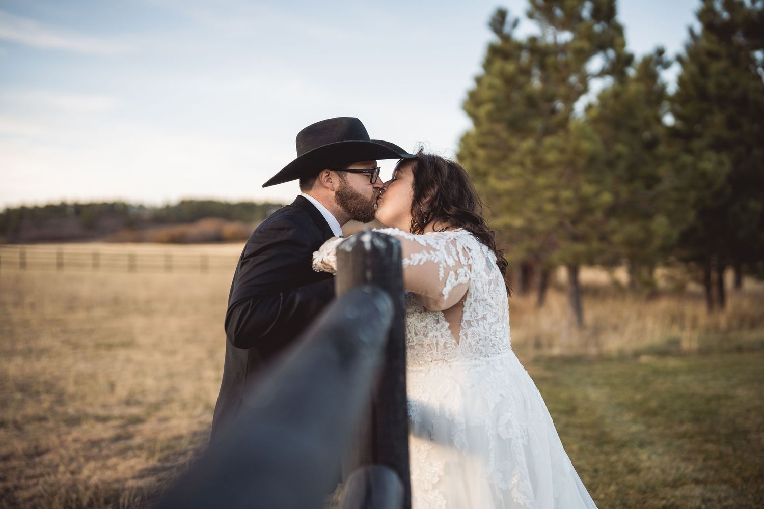Intimate wedding portraits in rustic outdoor setting with mountains and fence at golden hour.