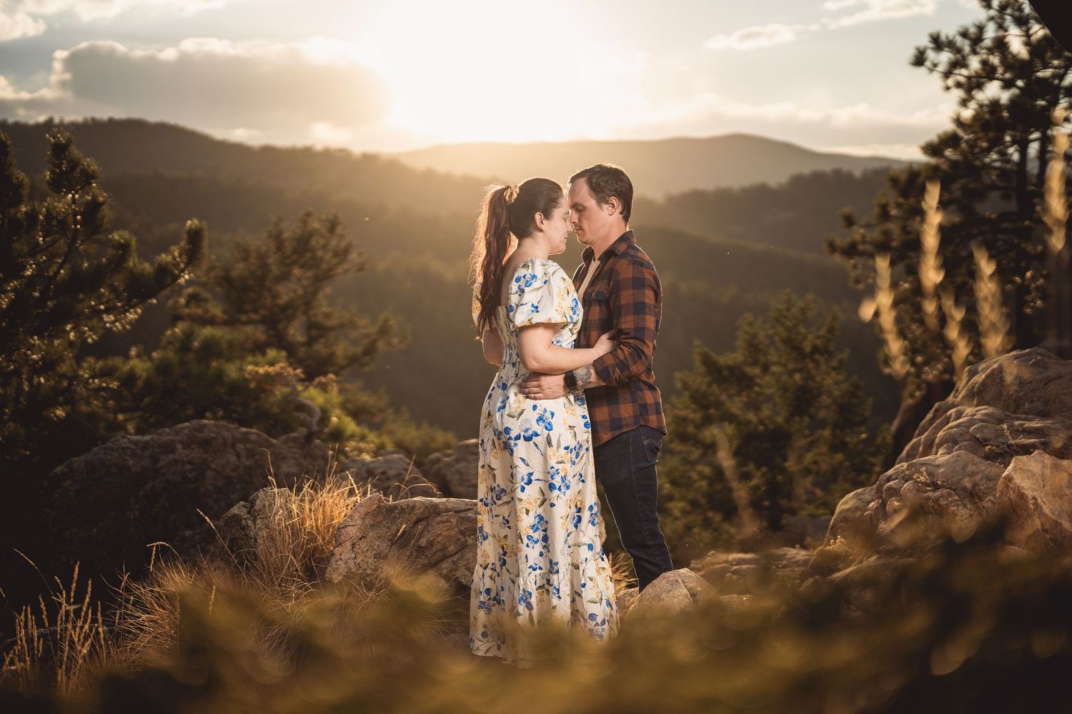 Couple sharing a romantic kiss at golden hour with stunning mountain and forest backdrop.