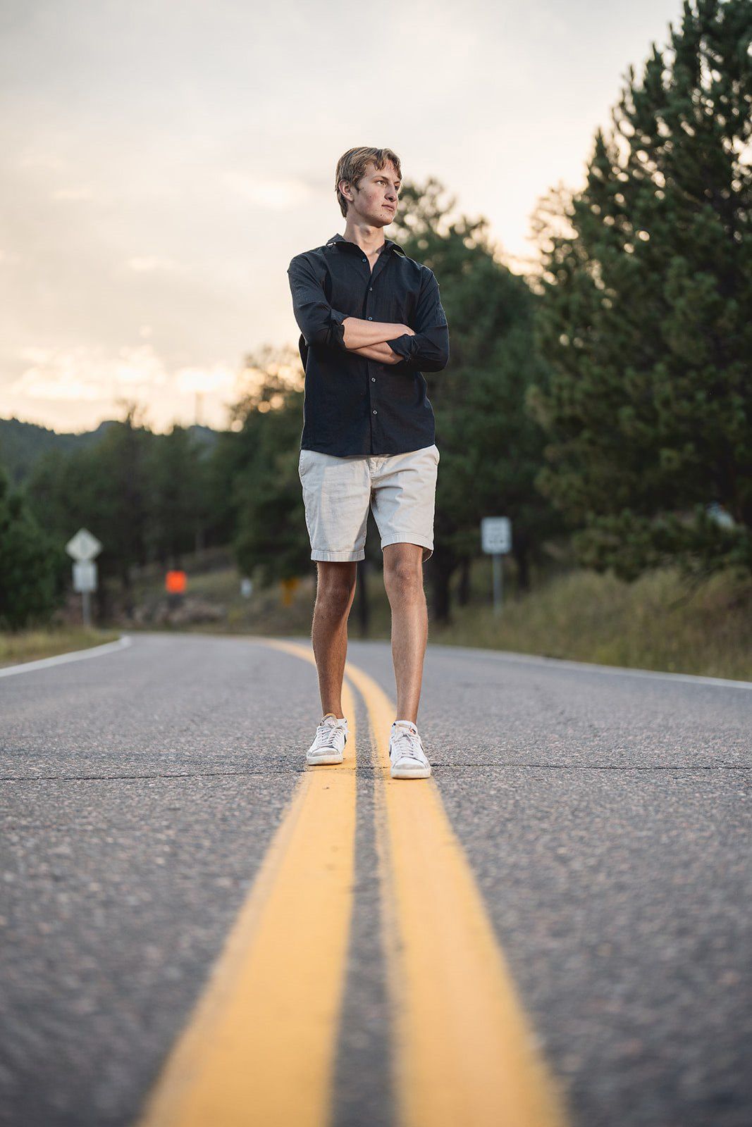 Young man with crossed arms standing on road centerline at sunset.