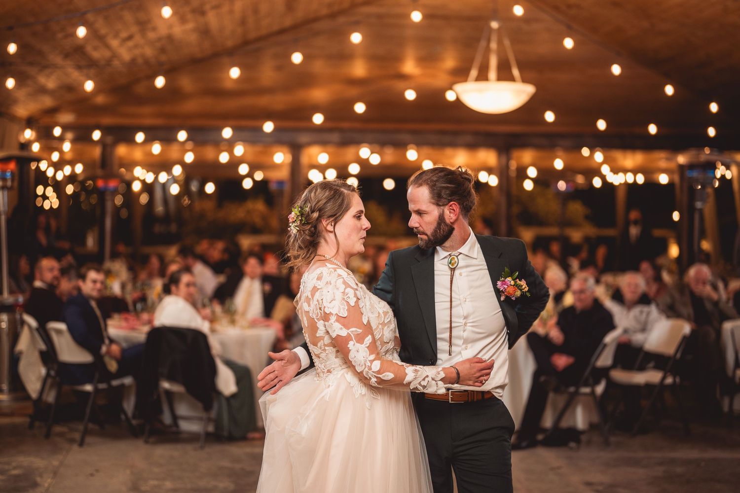 Wedding couple shares an intimate dance moment under warm lighting in a rustic reception space.