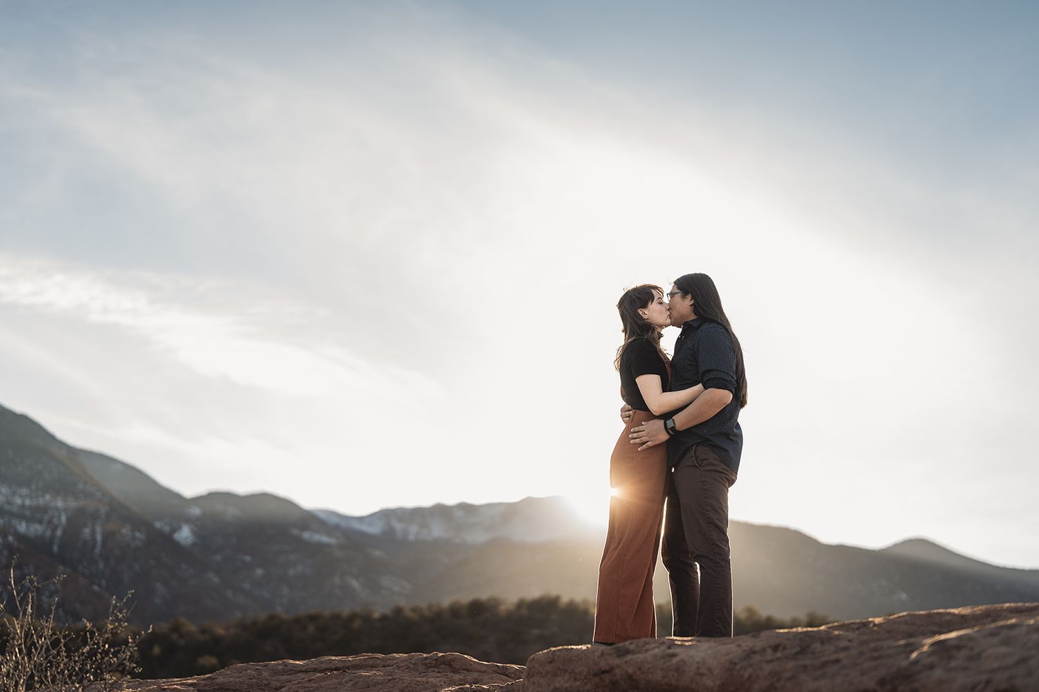 Loving couple embraces at sunset with mountain silhouettes creating a dramatic backdrop.