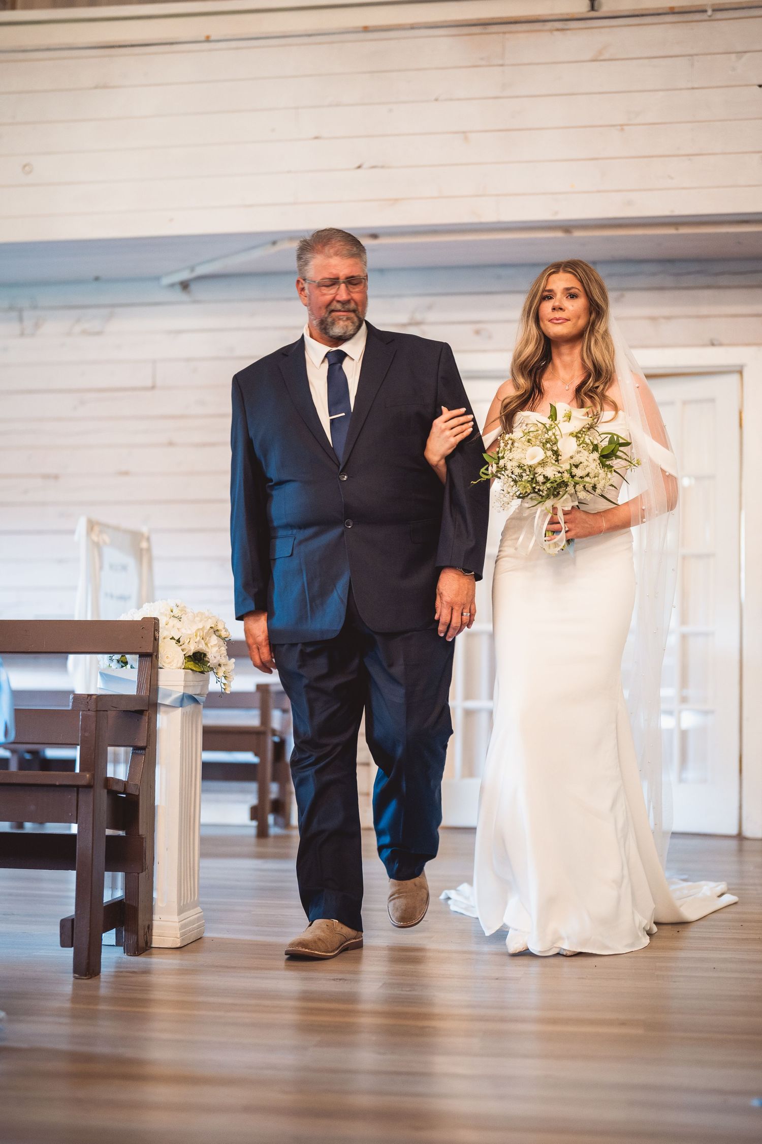 Wedding ceremony processional in elegant white chapel with hardwood floors and bright interior.