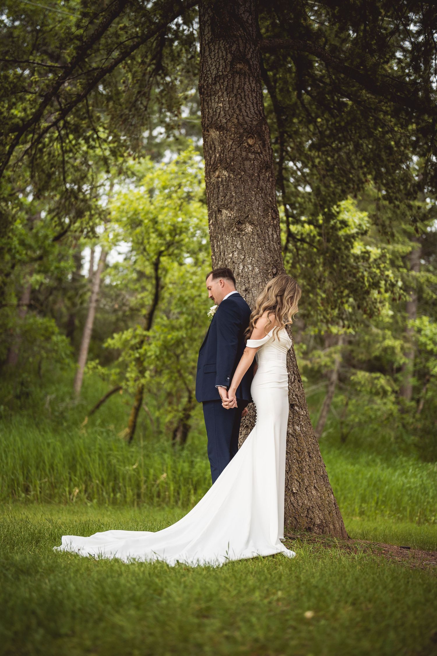 Wedding couple poses under large tree in lush green springtime setting.