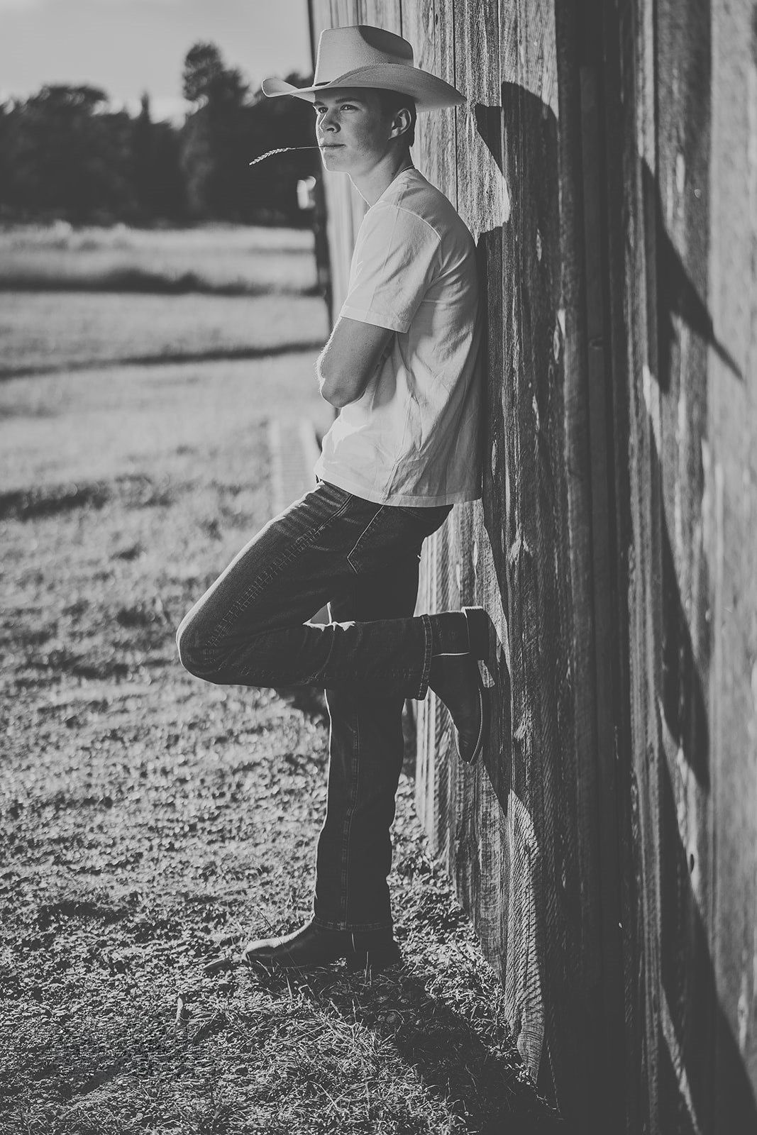 Black and white photo of person in cowboy hat leaning against wooden fence post.