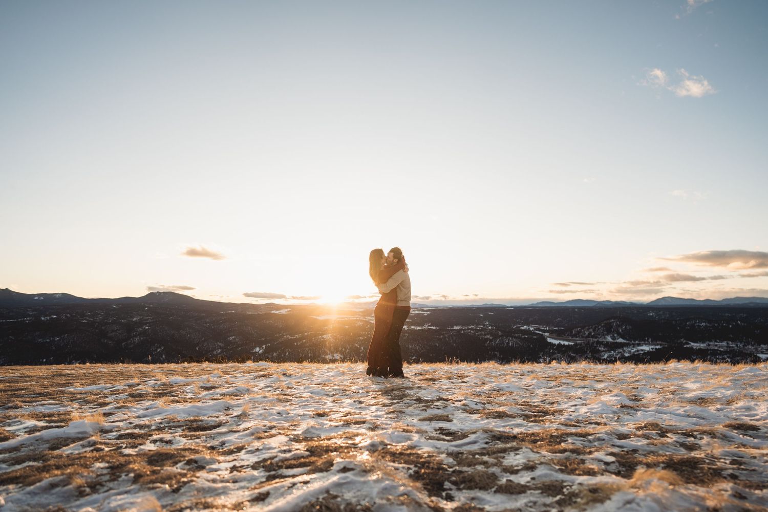 Panoramic winter landscape with figures silhouetted against a setting sun.