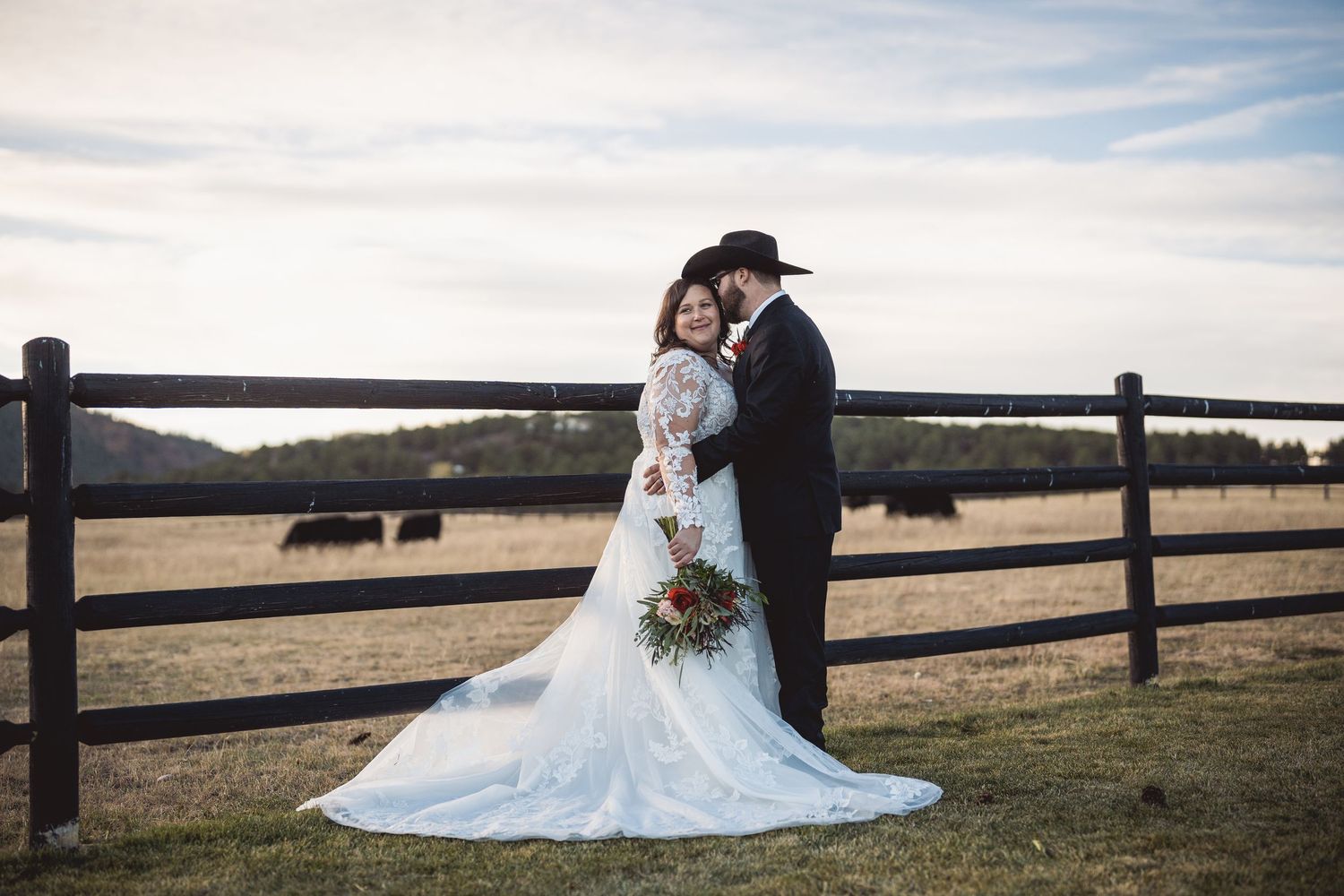 Beautiful wedding moment captured against natural landscape with wooden fence and rolling hills.