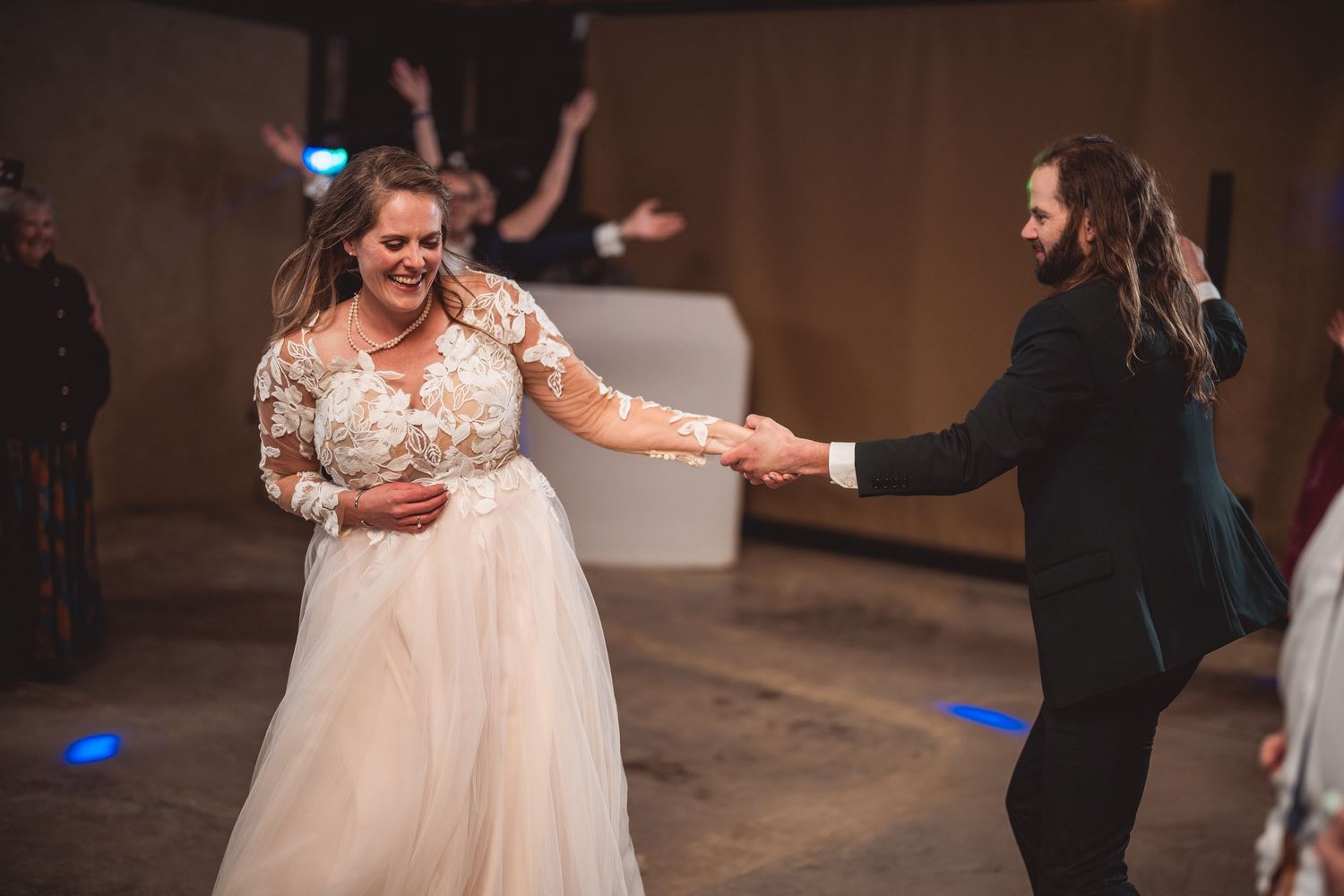 Wedding dance captured in a rustic venue with blue lighting accents and string lights overhead.