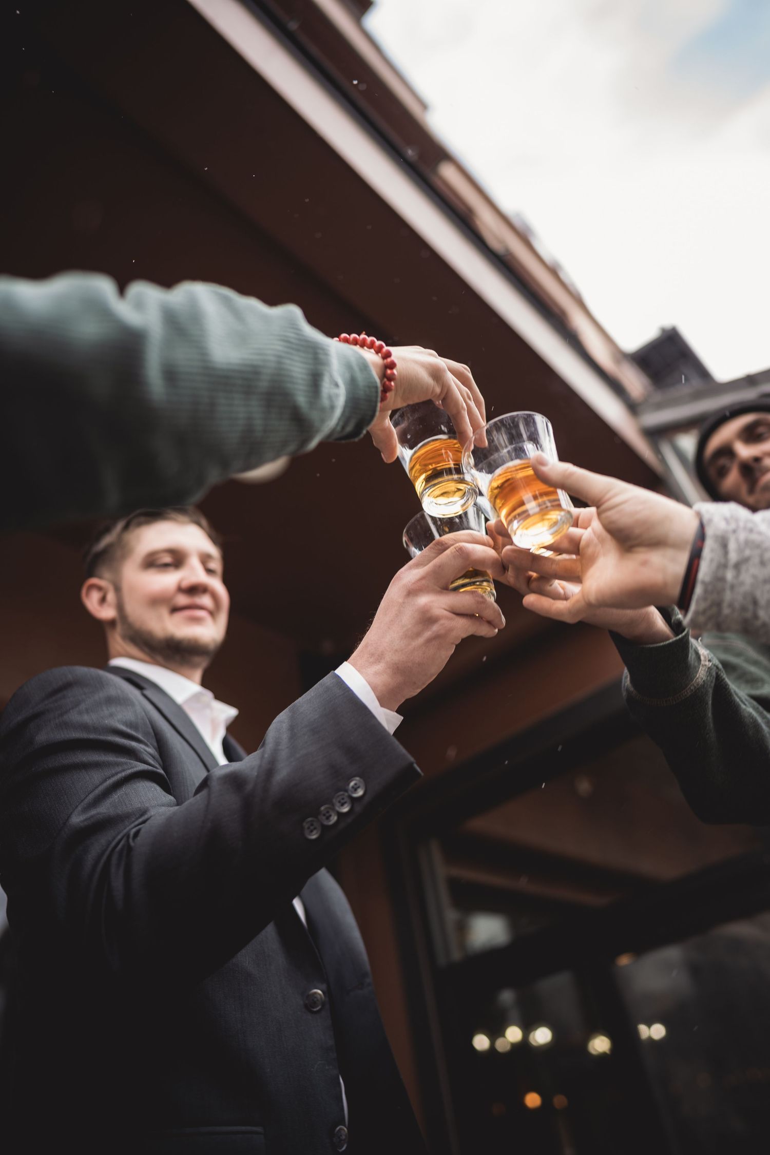 Group of men toasting with glasses of whiskey outdoors at a celebration or party event.