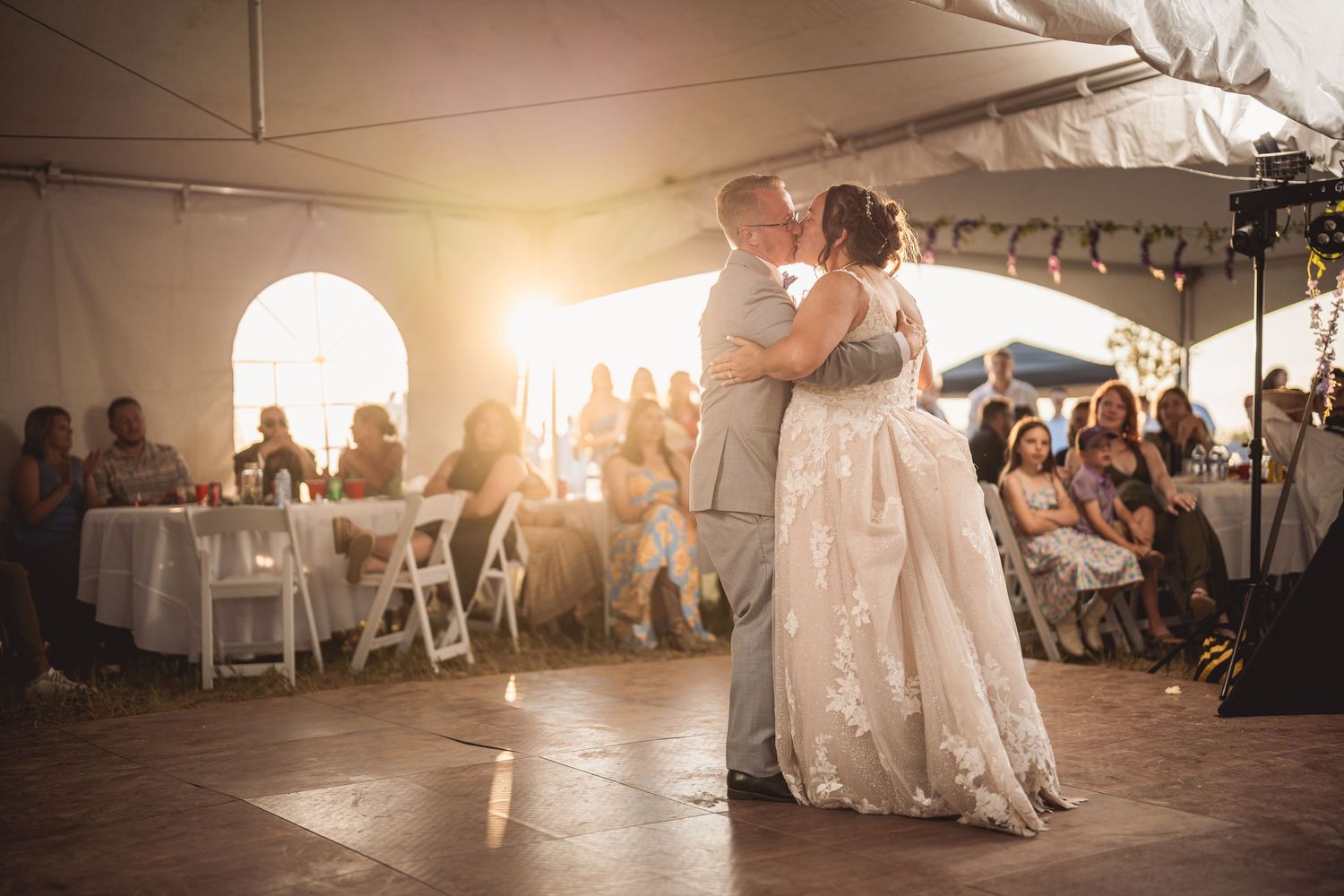 Bride and groom share first dance under a tent at golden hour wedding reception with guests seated around the dance floor.