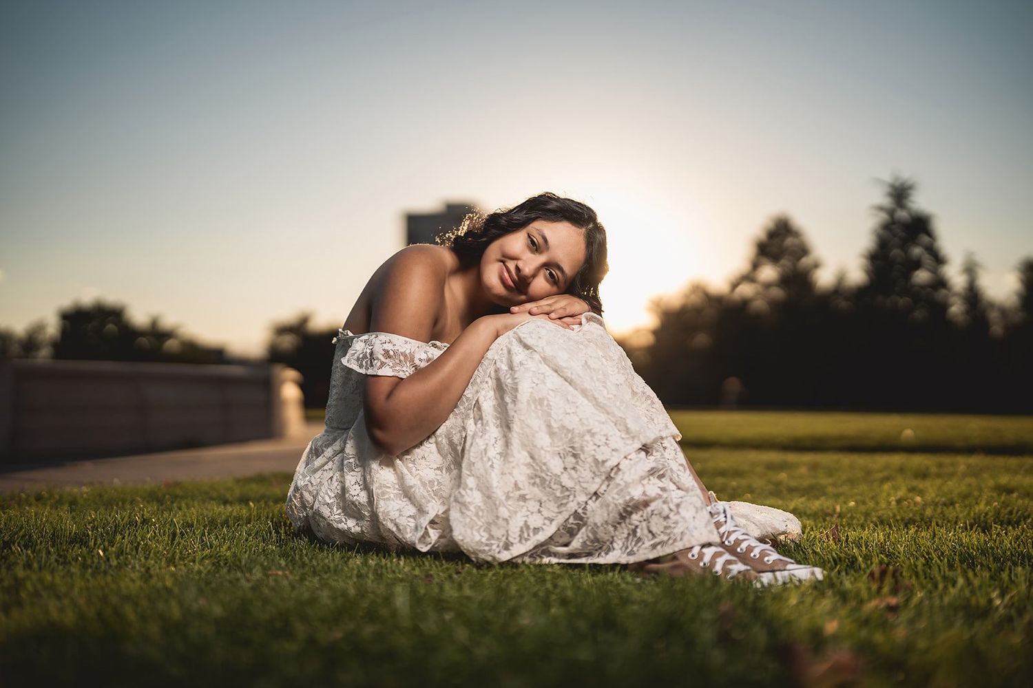 Person wearing white lace dress lying in a grassy field during golden hour sunset.