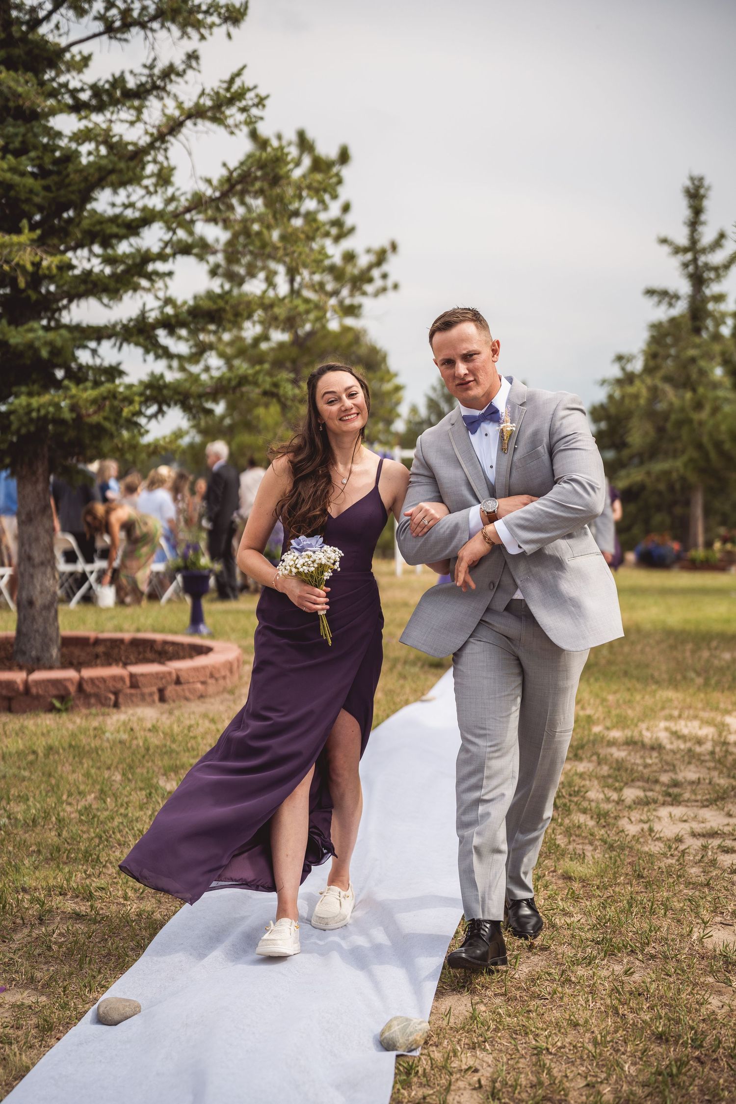 Wedding party members walking dramatically down white aisle runner outdoors.