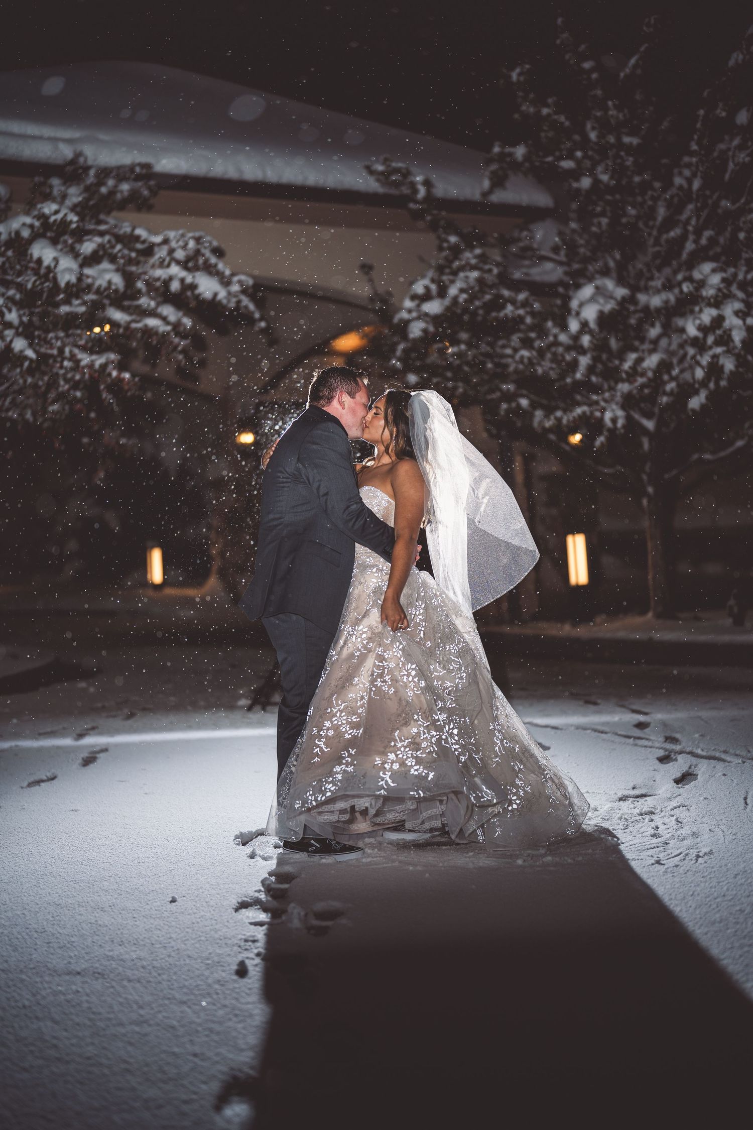 A dramatic wedding photo captured in the snow with warm lighting in the background.