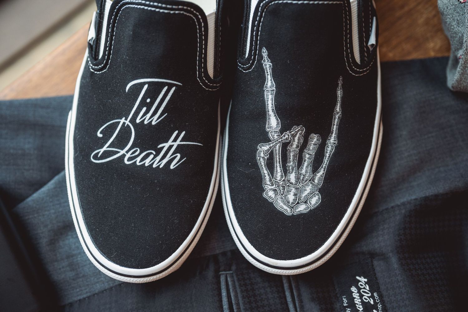 Black canvas shoes customized with white hand-drawn rock and roll symbols and text on a wooden surface.