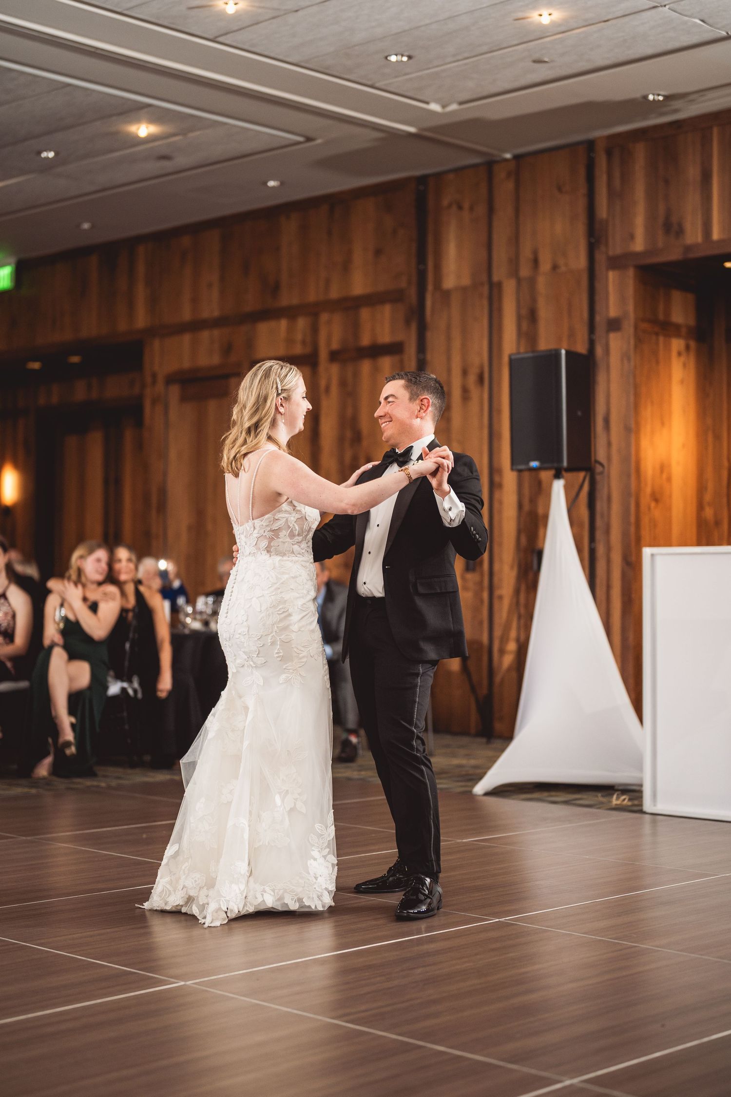 Newlyweds share their first dance in an elegant wood-paneled ballroom with mood lighting.