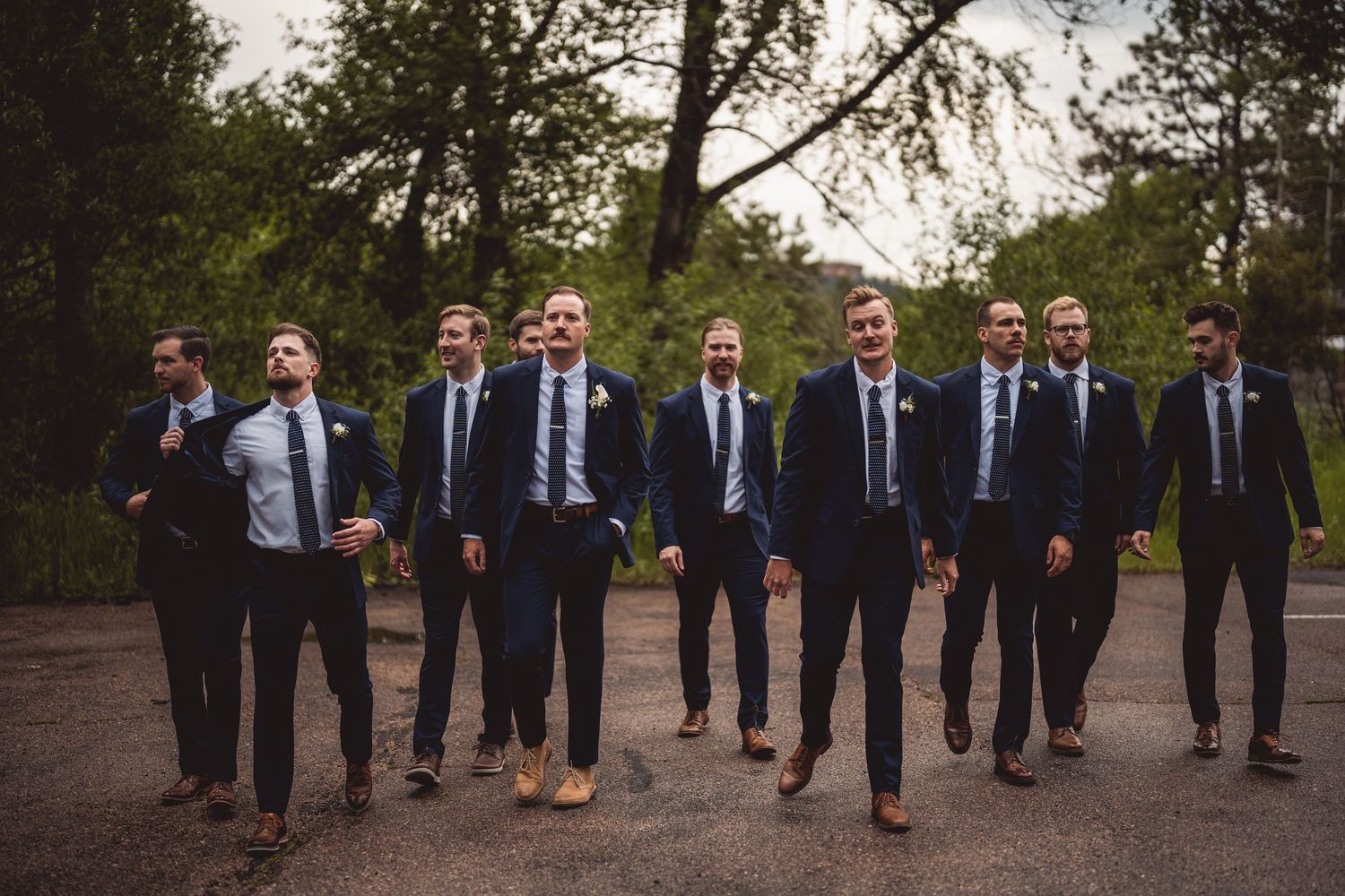 Groomsmen in navy suits walking together through an outdoor garden pathway.