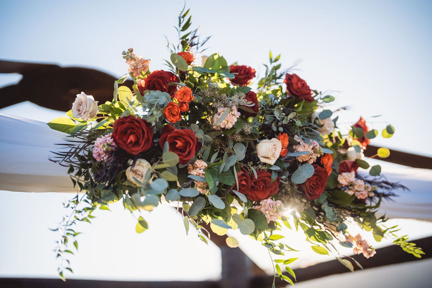 Elegant floral arrangement with red and white roses decorating an outdoor ceremony arch.
