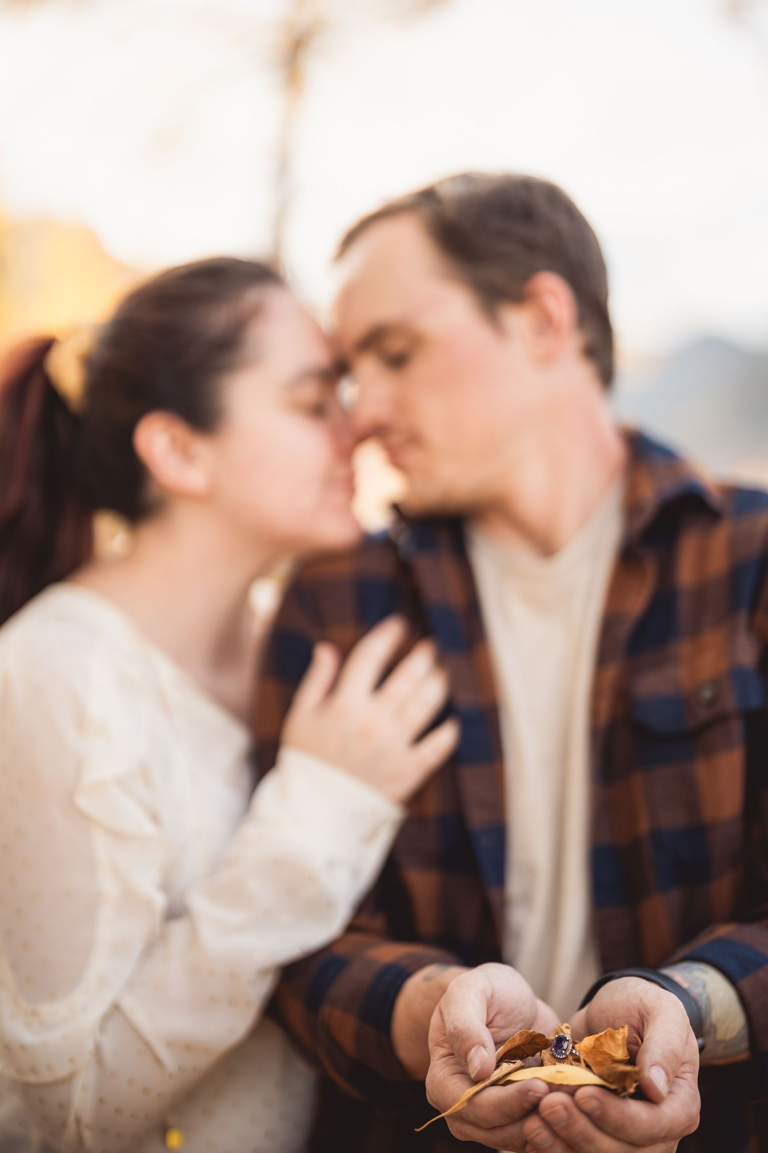 Intimate autumn photoshoot shows couple embracing with white sweater and plaid shirt.