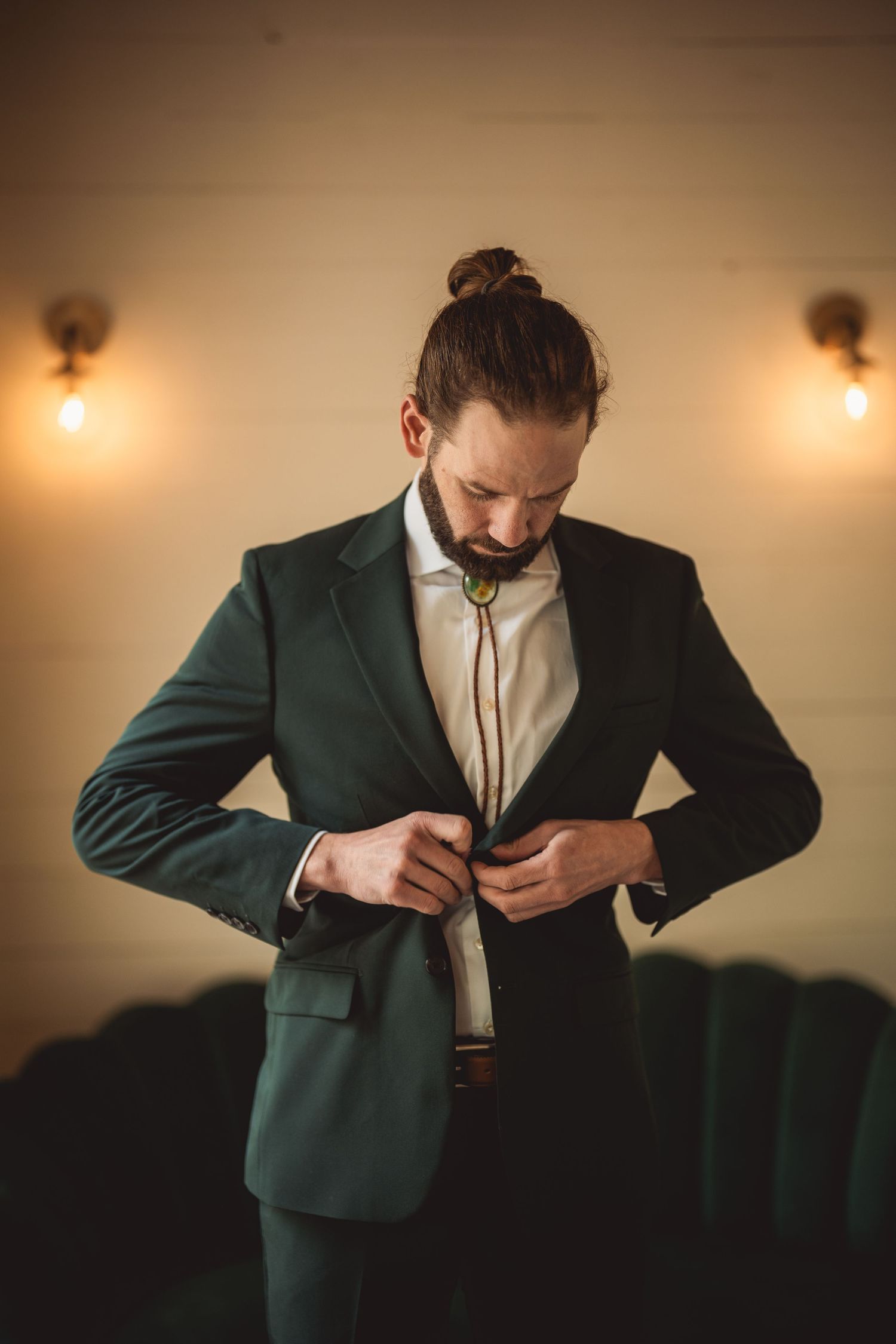 Person adjusting formal green jacket in warm indoor lighting.
