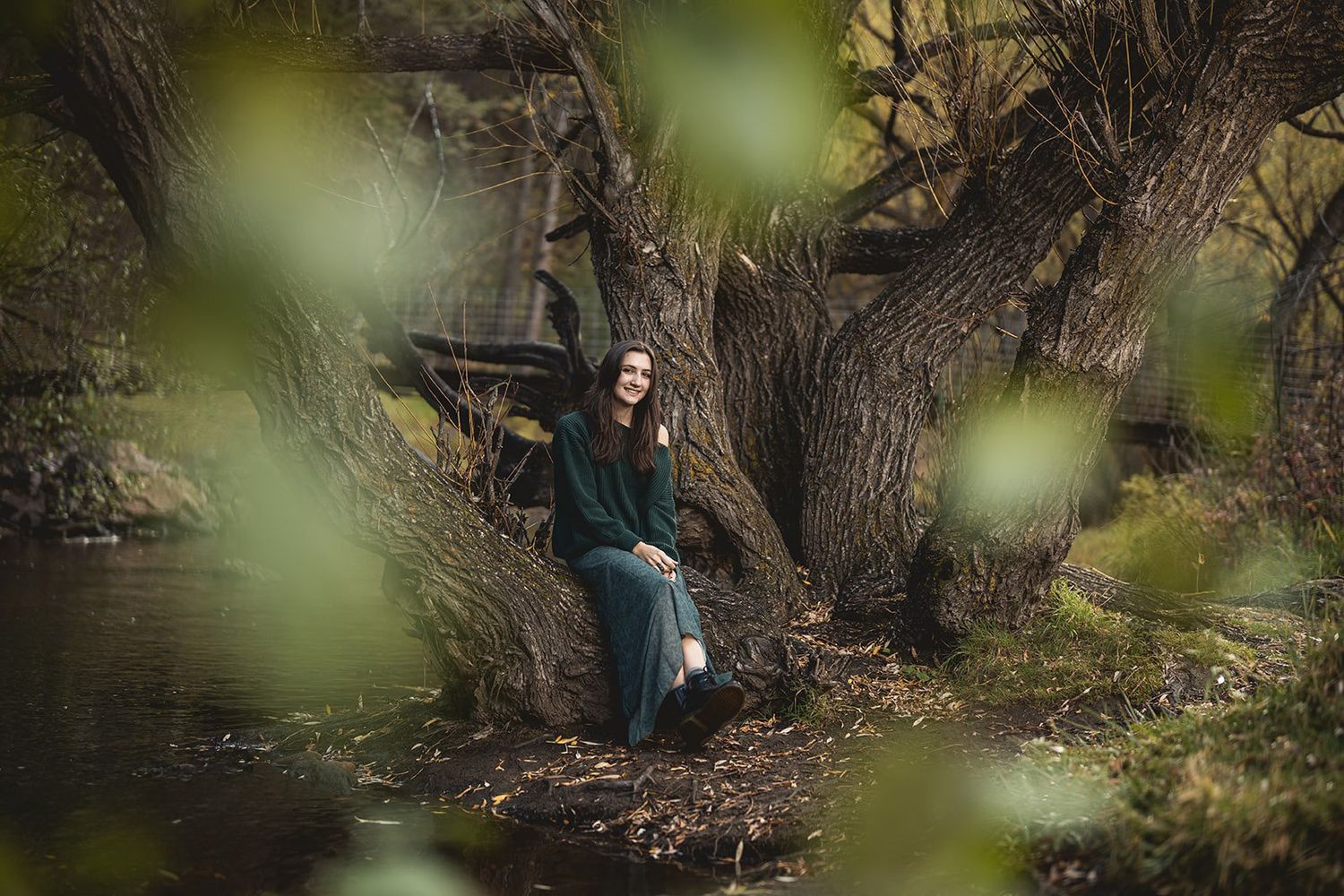 Artistic portrait through leaves and branches near a wooded riverbank.