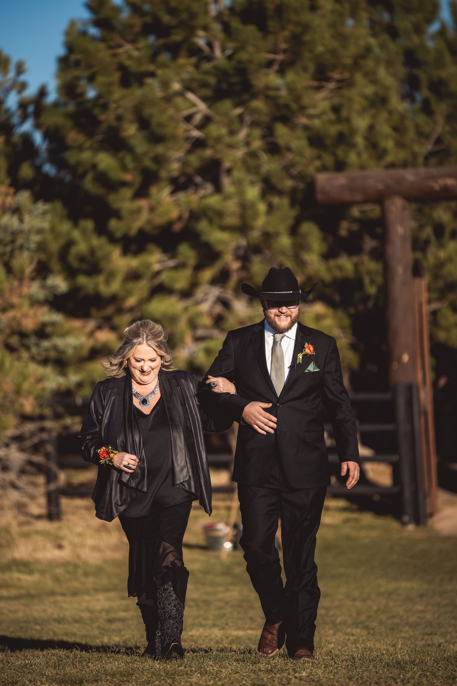 Wedding party walking across green lawn with pine trees in background.