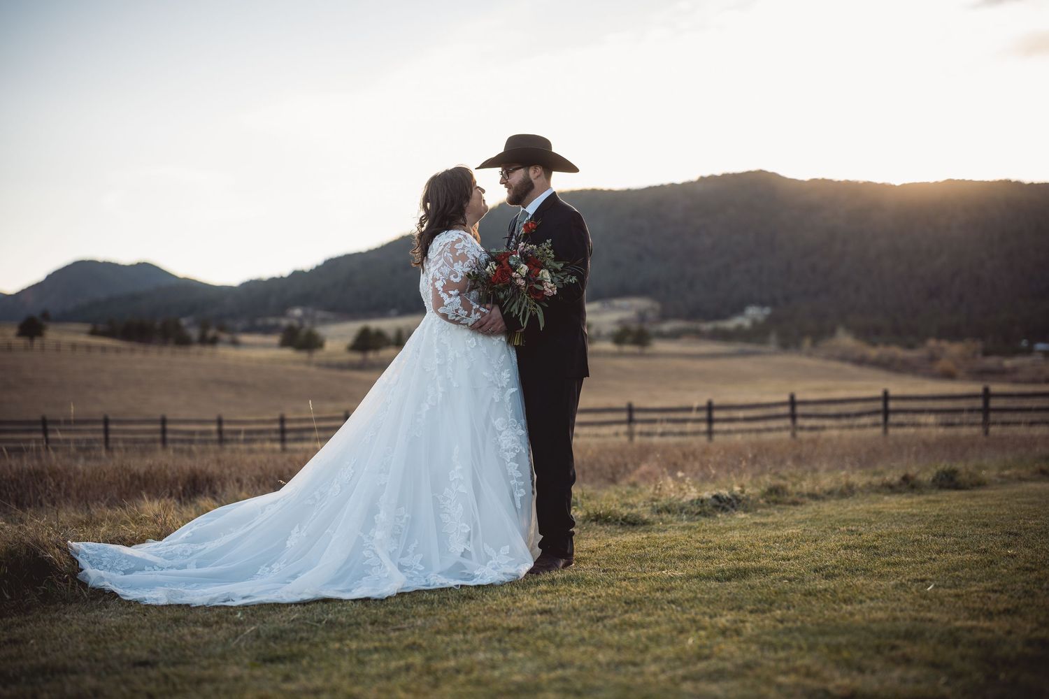 Sunset mountain wedding portrait with couple embracing near rustic fence.