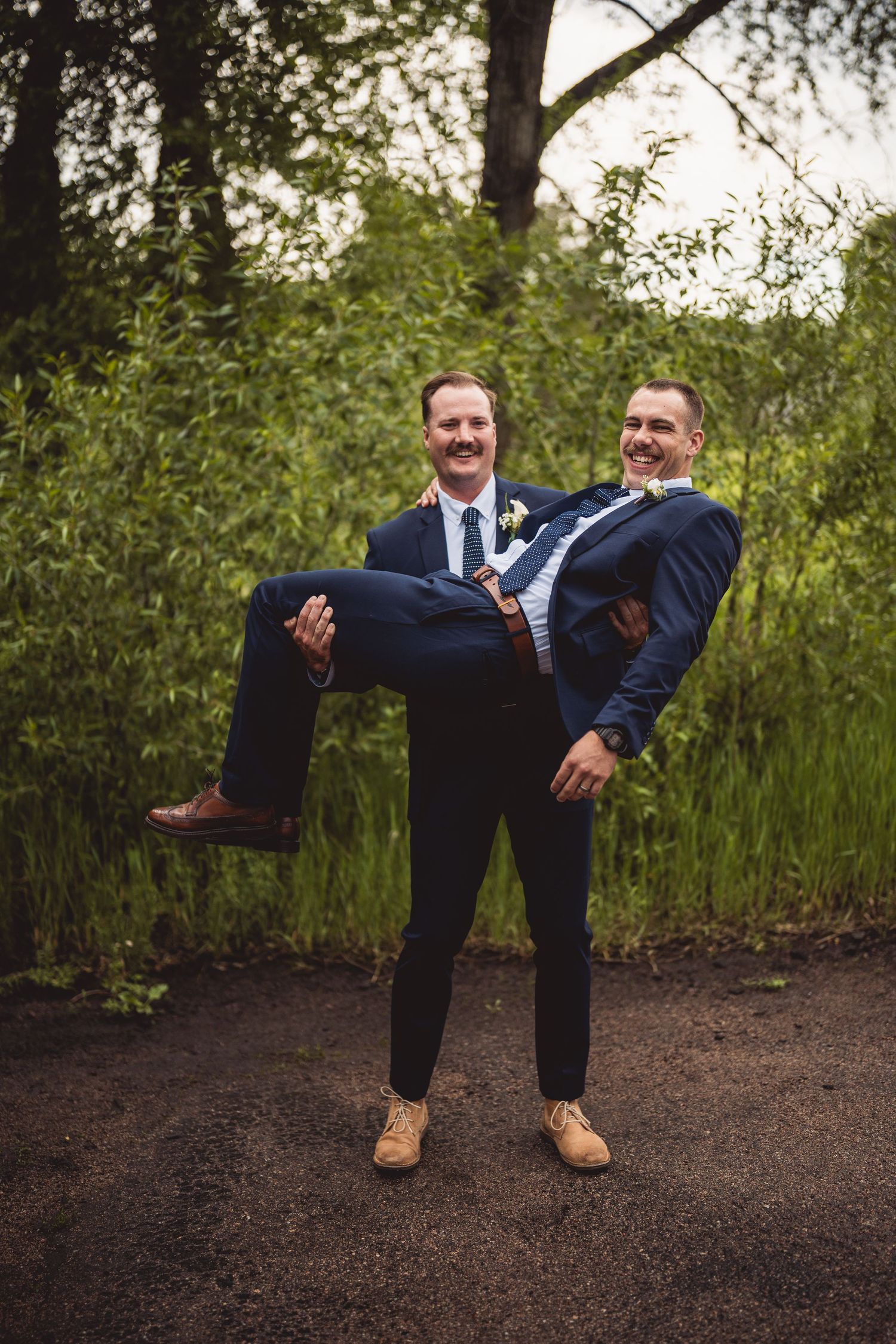 Groomsmen perform playful leg-lifting poses against natural woodland backdrop.
