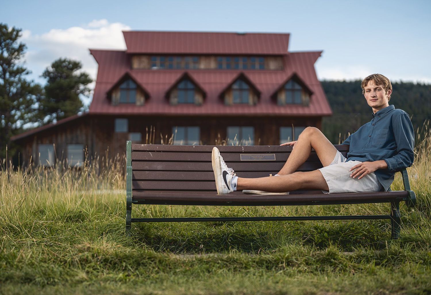 Young man relaxing on outdoor bench with rustic mountain lodge in background.