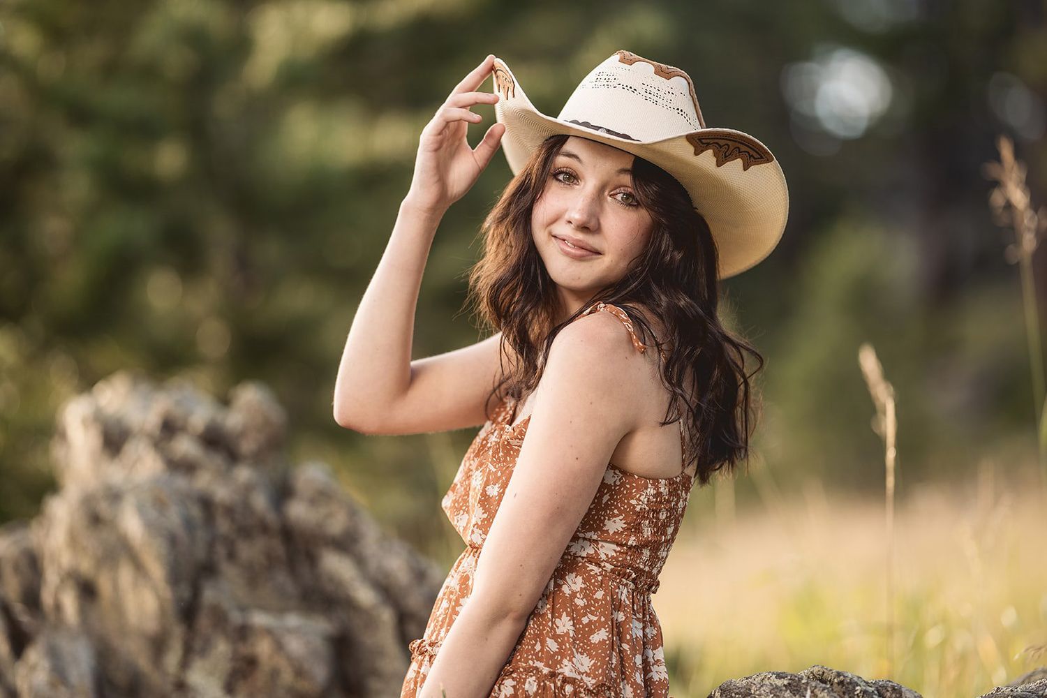 Person in floral dress and sun hat posing in a sunlit meadow.