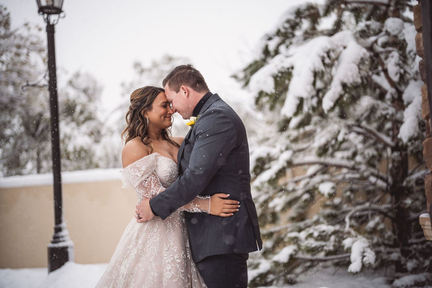 Wedding couple embraces during their winter photo session with snow-covered trees and lamp post.