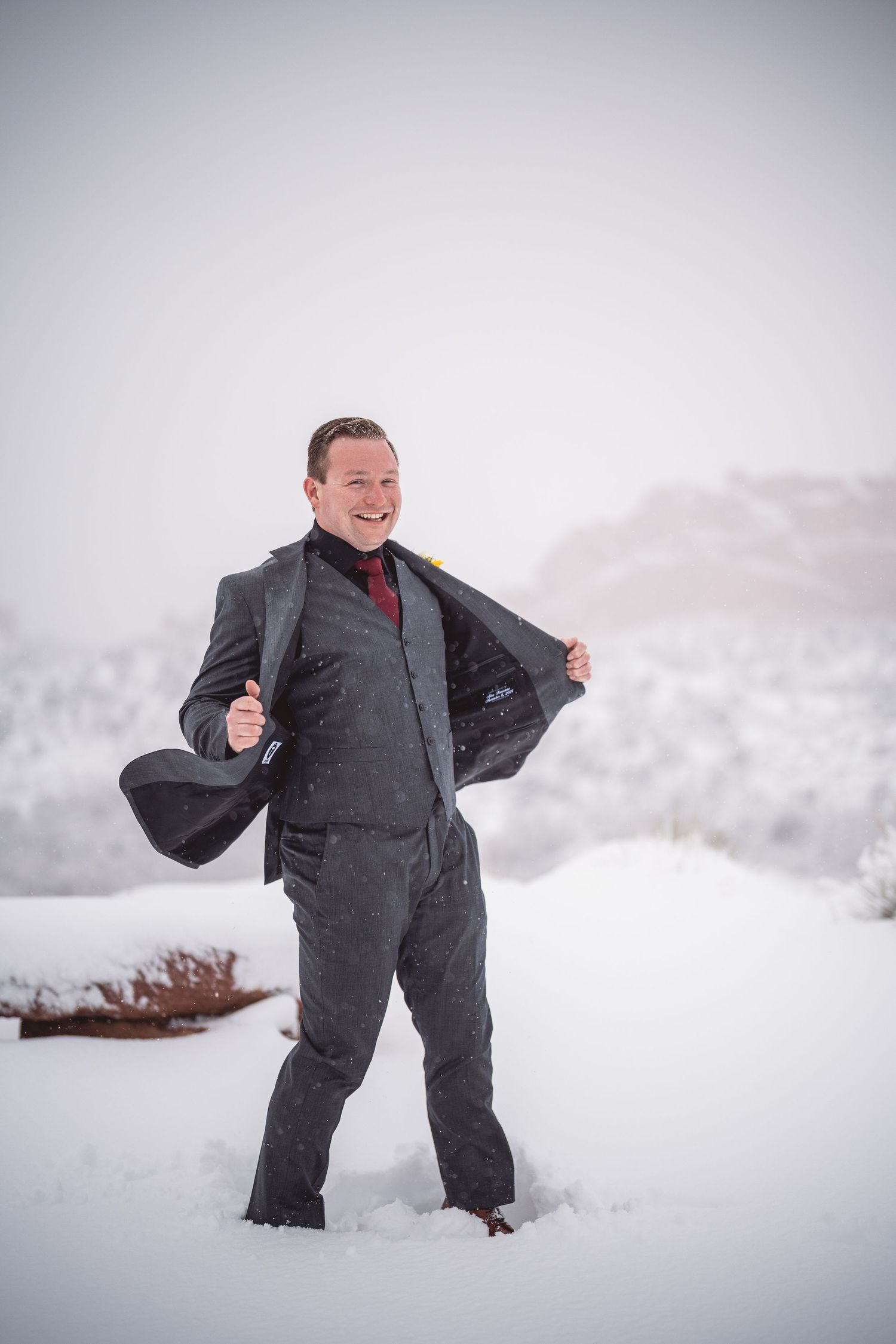 Person in grey suit stands playfully in deep winter snow during a photoshoot.