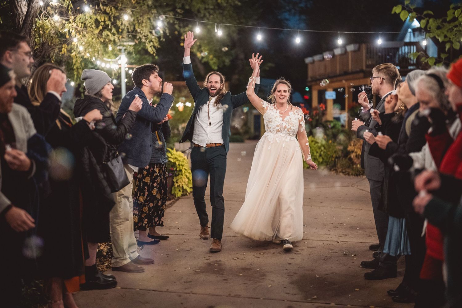 Wedding party and guests form an aisle outdoors at night while celebrating the newlyweds.