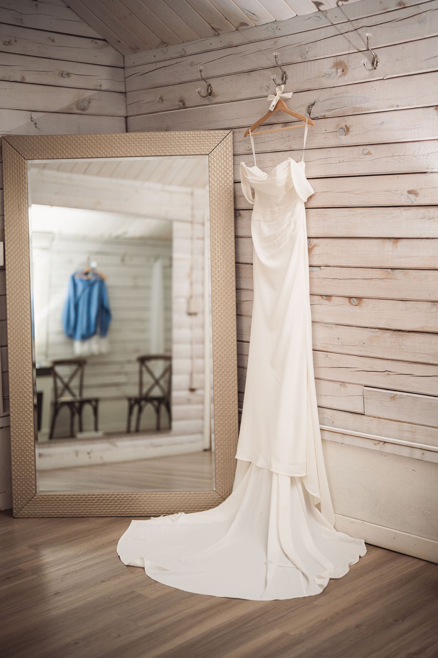 Wedding dress displayed in rustic wooden room with mirror and elegant decor.