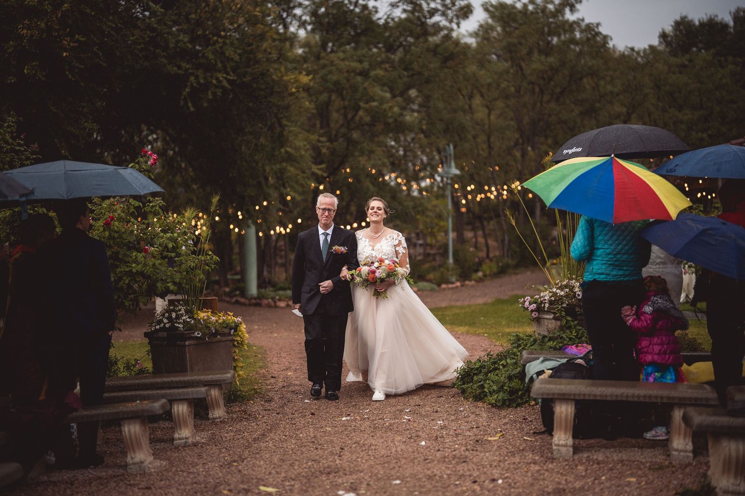 Outdoor wedding ceremony path decorated with umbrellas and string lights at dusk.