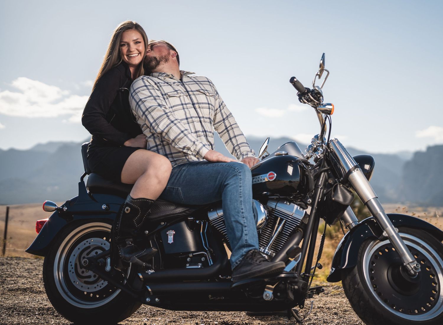 A couple sitting together on a Harley Davidson motorcycle with mountains in the background.