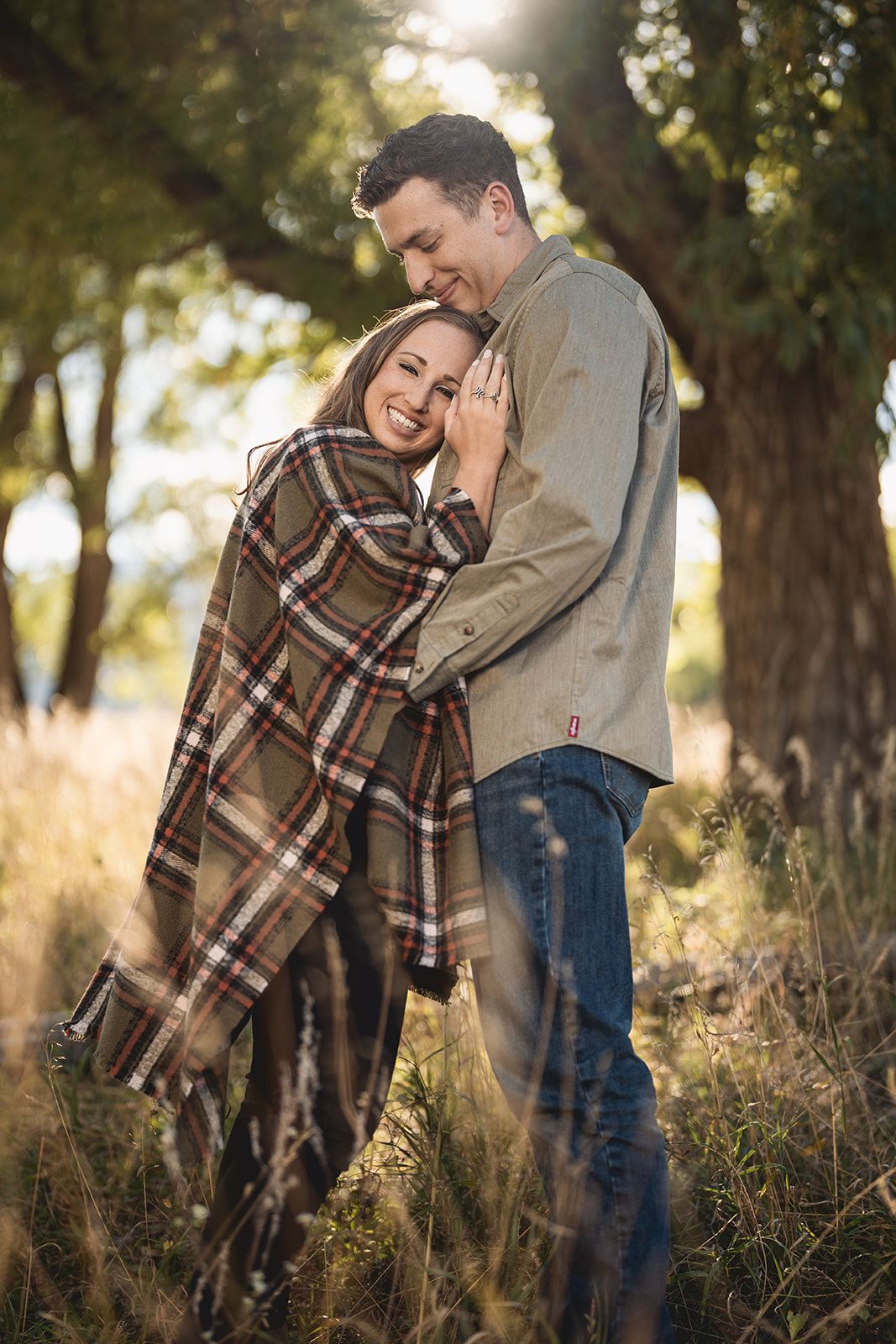 Couple wrapped in plaid blanket share intimate moments during sunset engagement session.