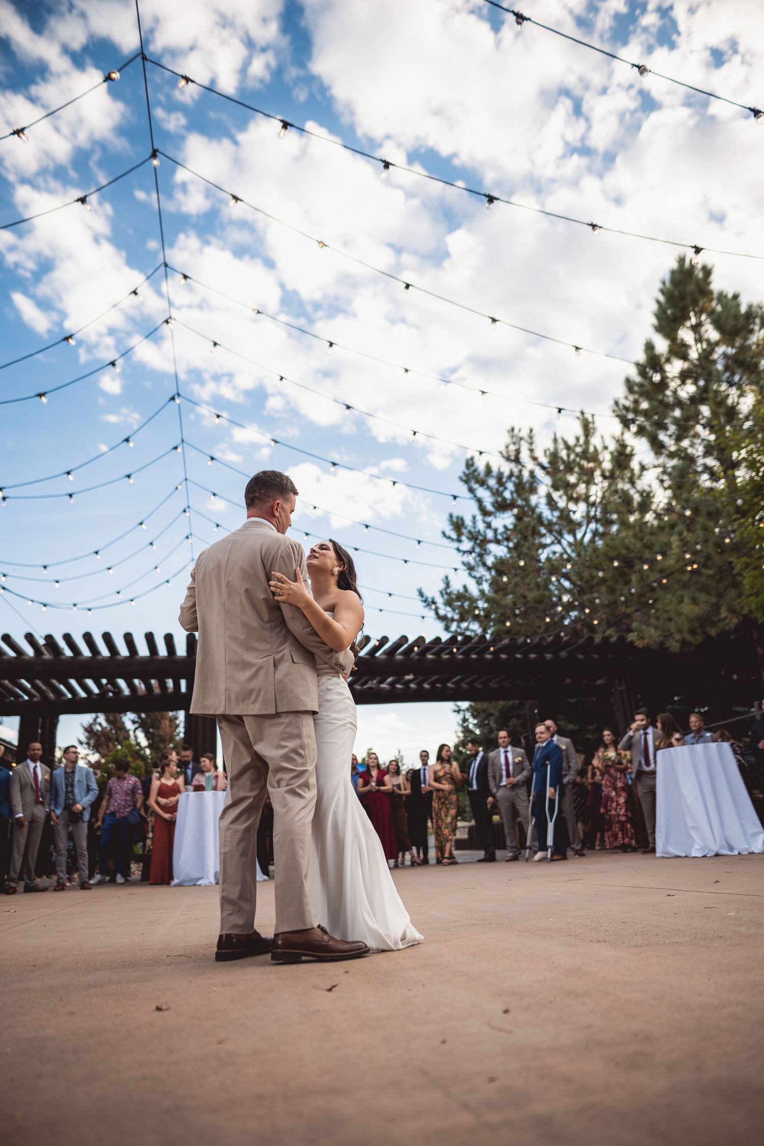 First dance at outdoor wedding reception under twinkling string lights at sunset.