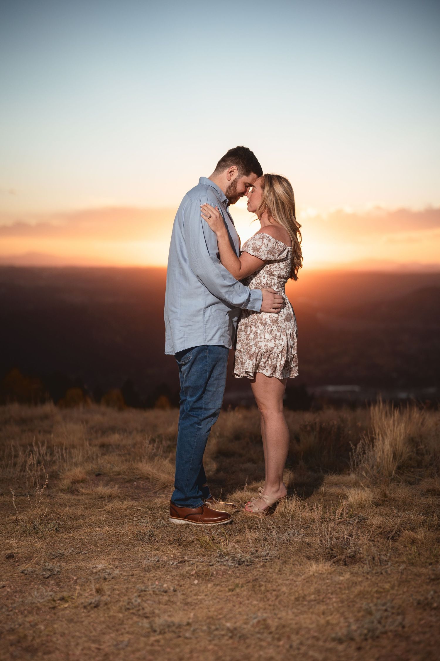A couple poses together at sunset on a hilltop in a romantic outdoor engagement photoshoot.