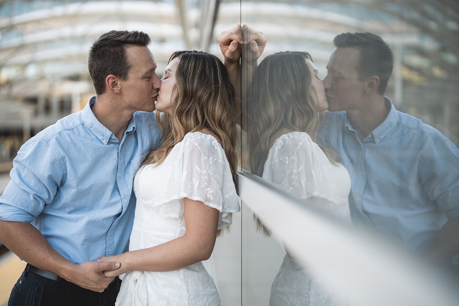 Couple shares intimate moment against reflective glass building exterior.