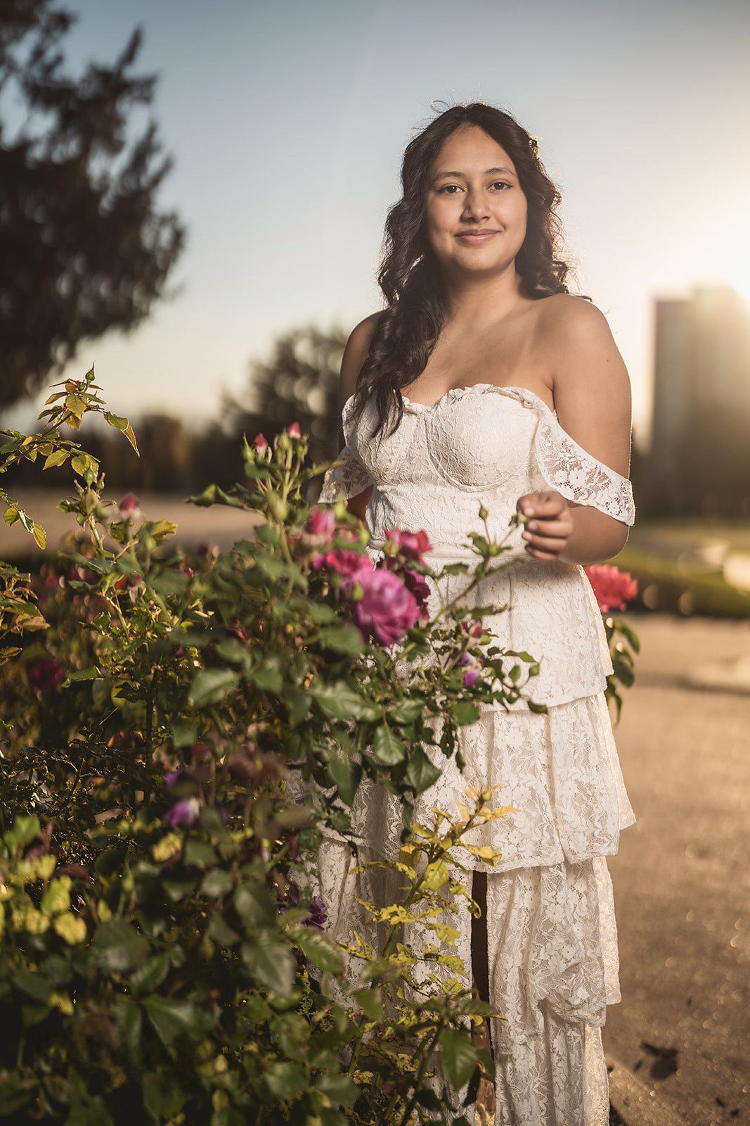 Garden portrait with pink roses and a layered white dress at sunset.