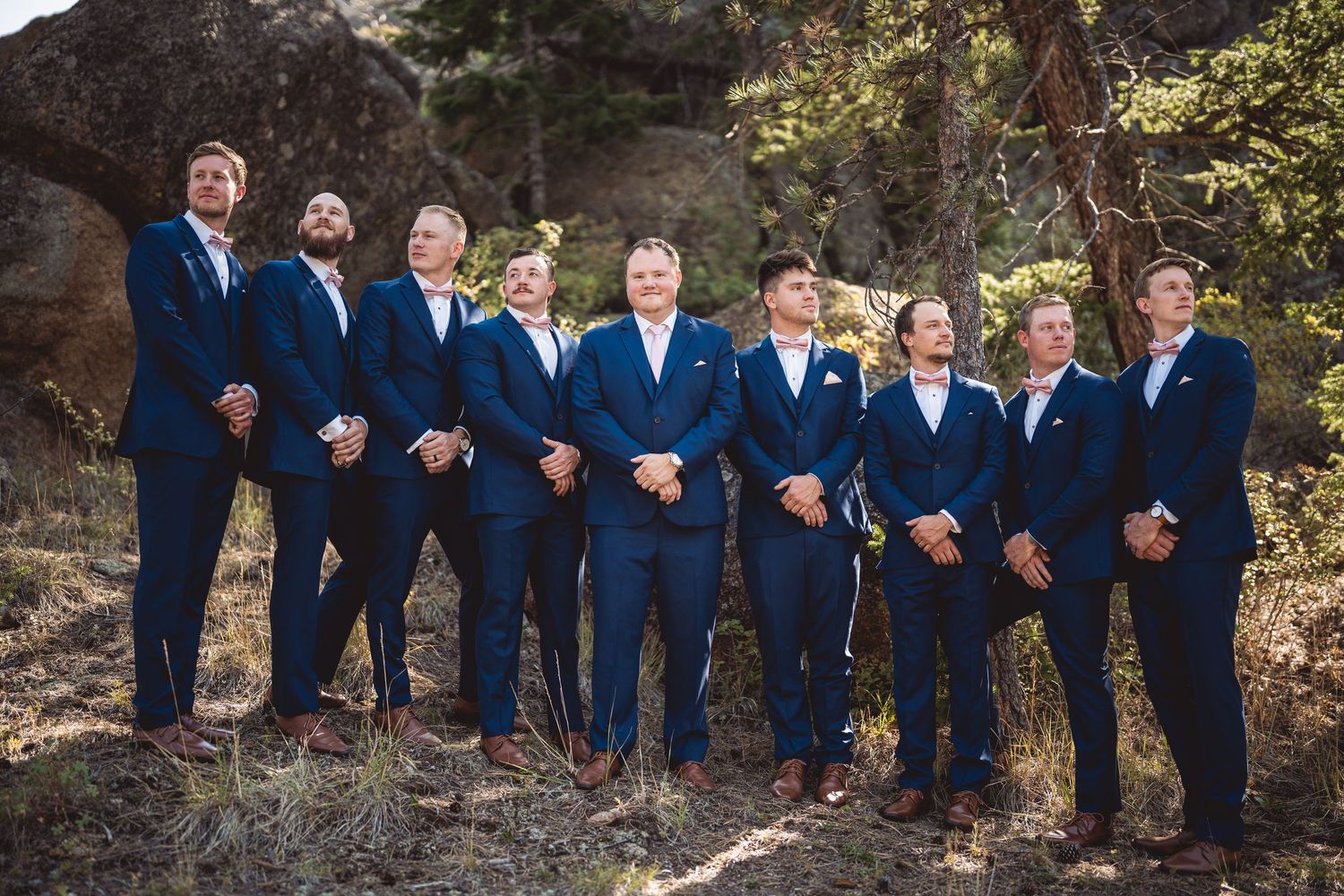Groomsmen in navy blue suits pose together on a wooded mountain path.