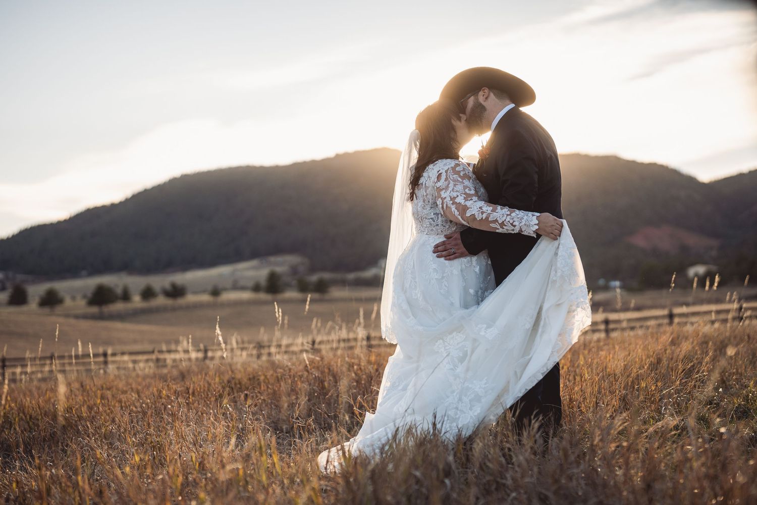 Panoramic view of a wedding couple's photo session in a mountain field at sunset.